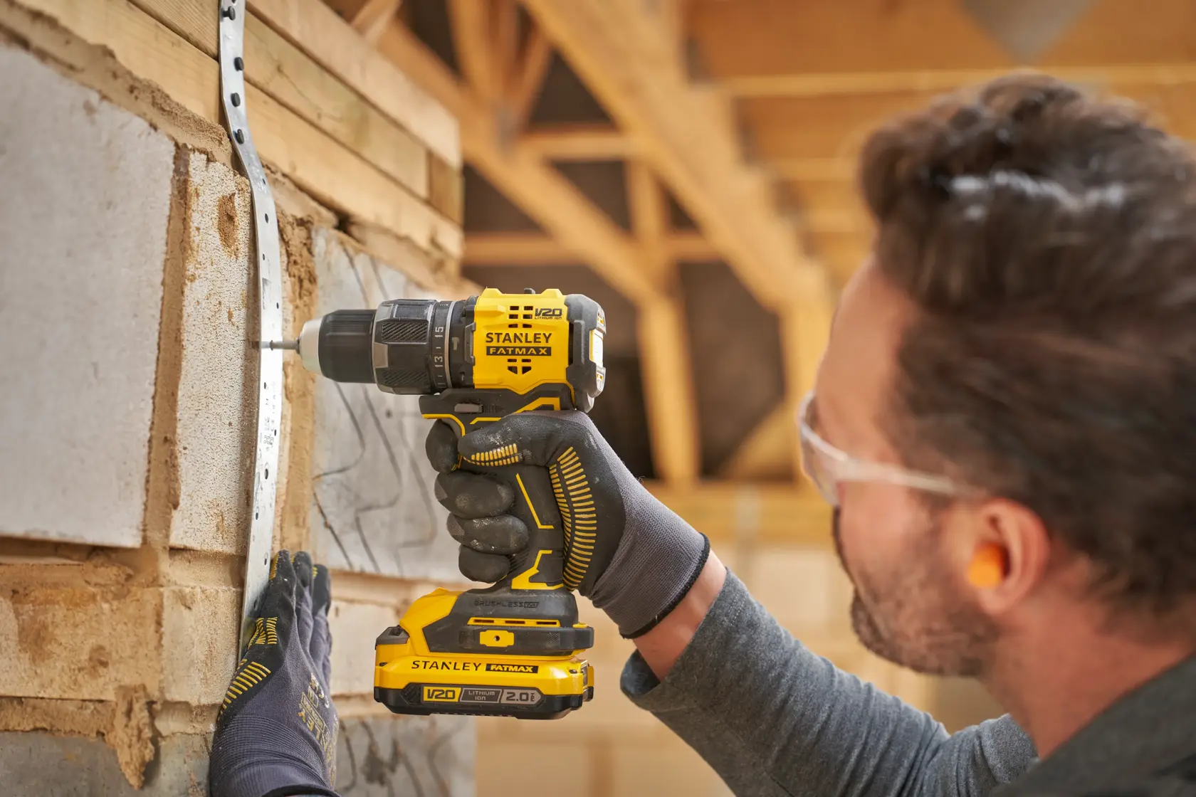 STANLEY SFMCD716B-XJ perceuse sans fil utilisée, vue latérale, perçage dans un mur avec batterie V20, homme avec gants.