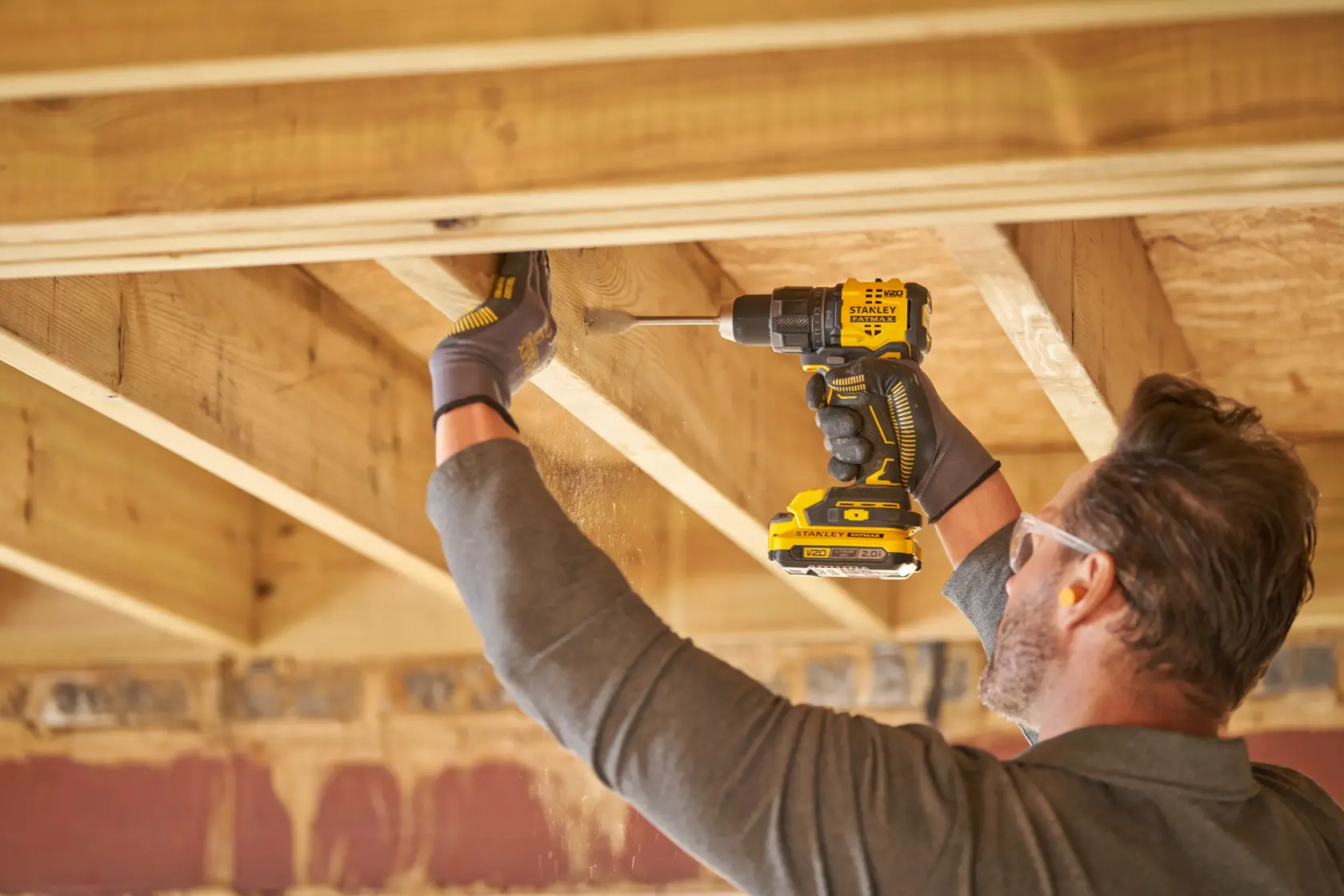 STANLEY SFMCD716B-XJ perceuse sans fil utilisée par une personne perçant des poutres en bois en intérieur, vue latérale.