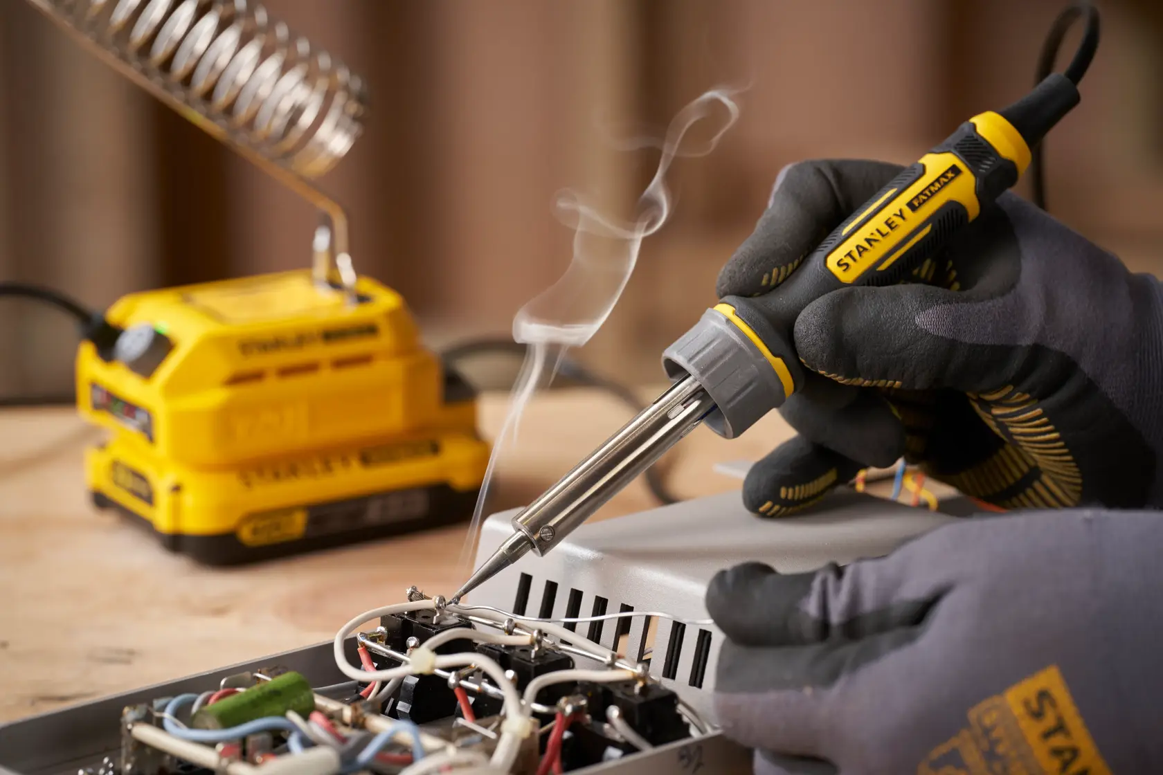 Foto del saldatore STANLEY SFMCE040B in uso, mano guantata salda componenti elettronici su una scheda.