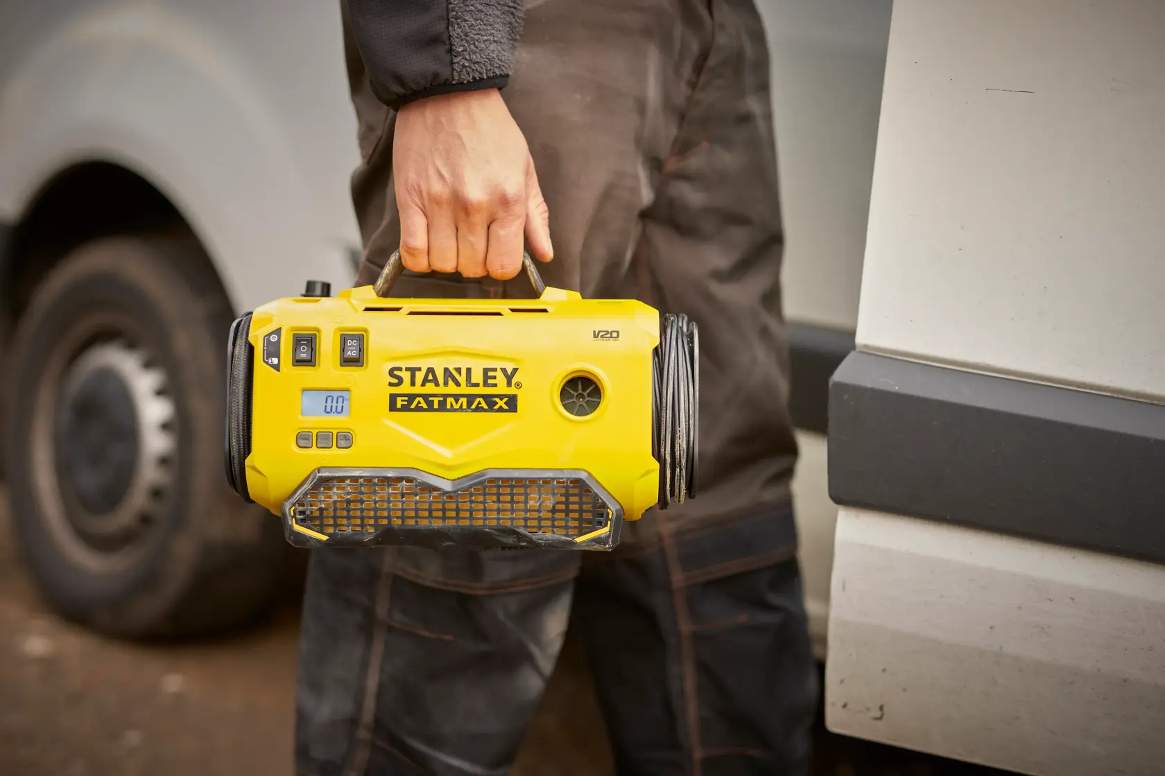 Gonfleur Stanley SFMCE520B portable jaune tenu par la poignée, utilisé à l'extérieur près d'un véhicule.