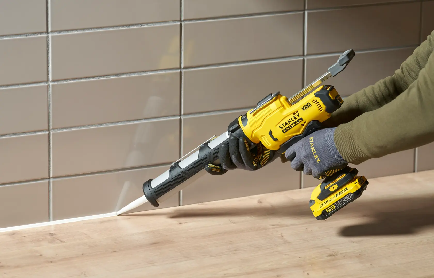 STANLEY SFMCE600B pistolet à calfeutrer sans fil utilisé pour sceller un joint entre un plan de travail en bois et un mur carrelé.
