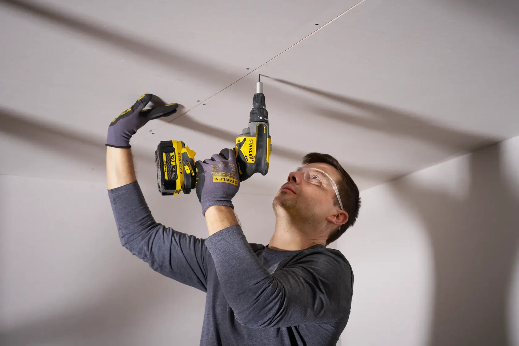 Visseuse à chocs STANLEY SFMCF600B utilisée pour fixer des vis dans un plafond en plaques de plâtre, vue en intérieur rapprochée.