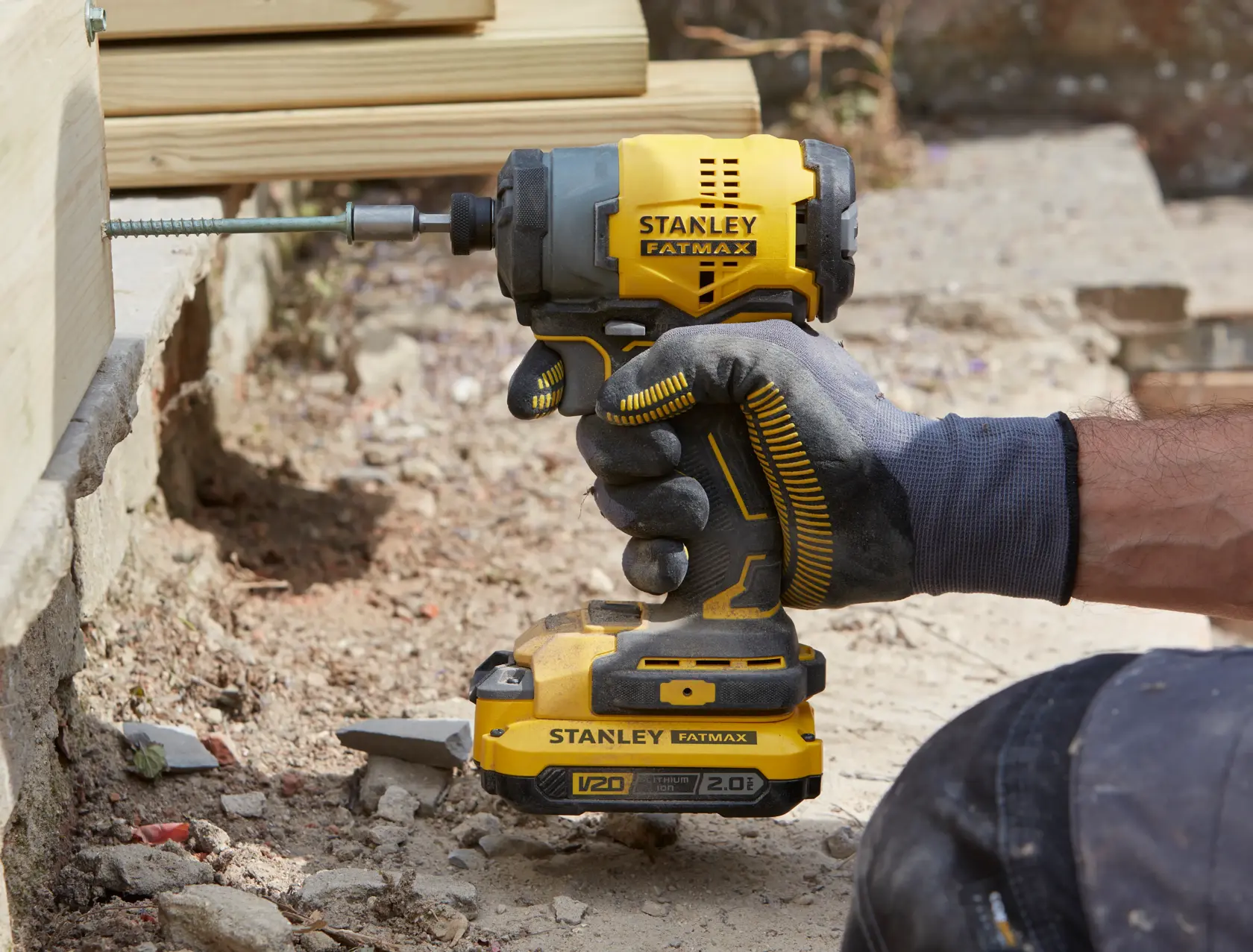 Stanley SFMCF810B tournevis à impact tenu par une main gantée, vissage dans du bois, environnement extérieur.