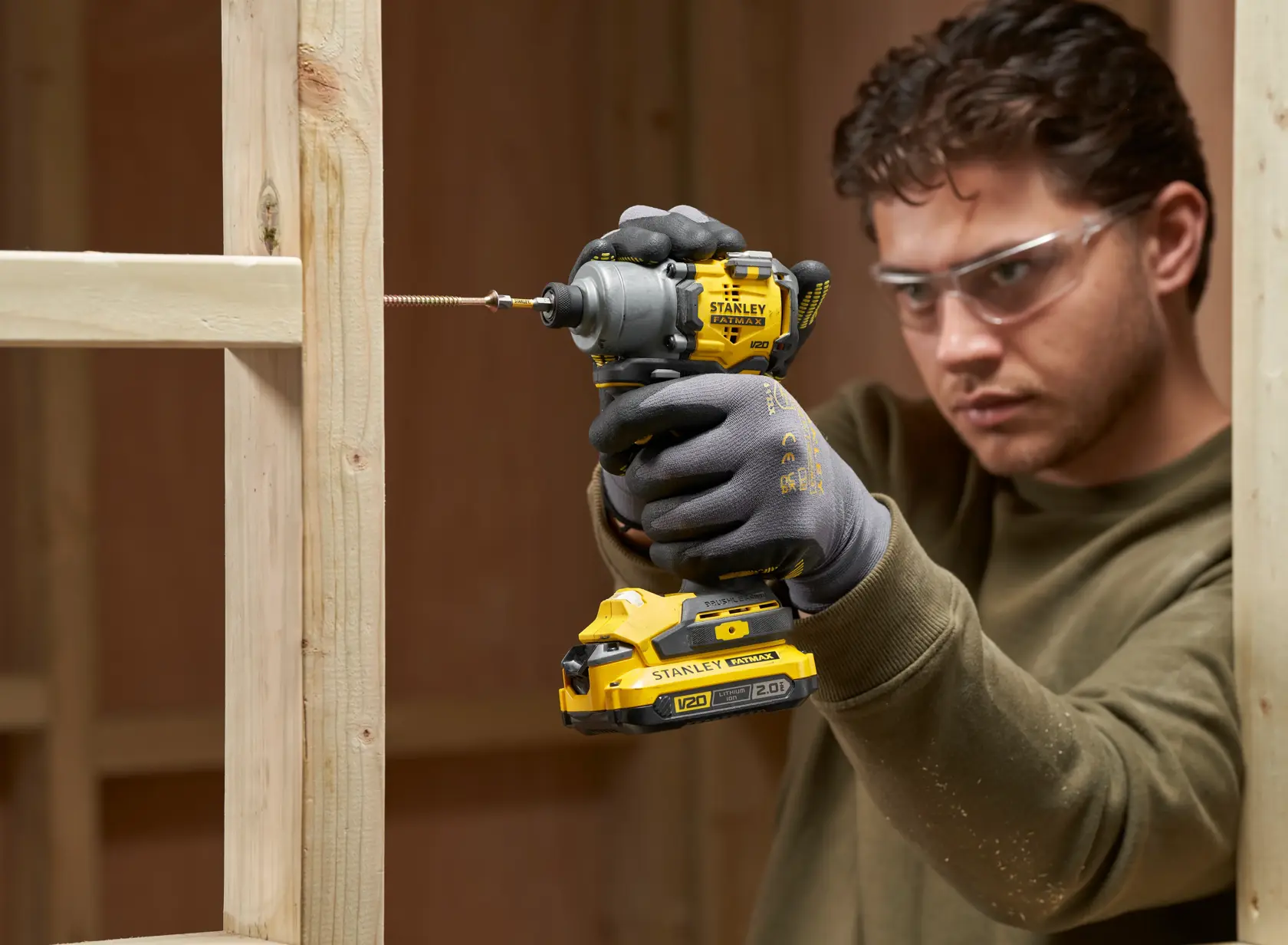 Photo of STANLEY SFMCF830D2K impact driver being used to drive a screw into wood framing, user wearing work gloves.