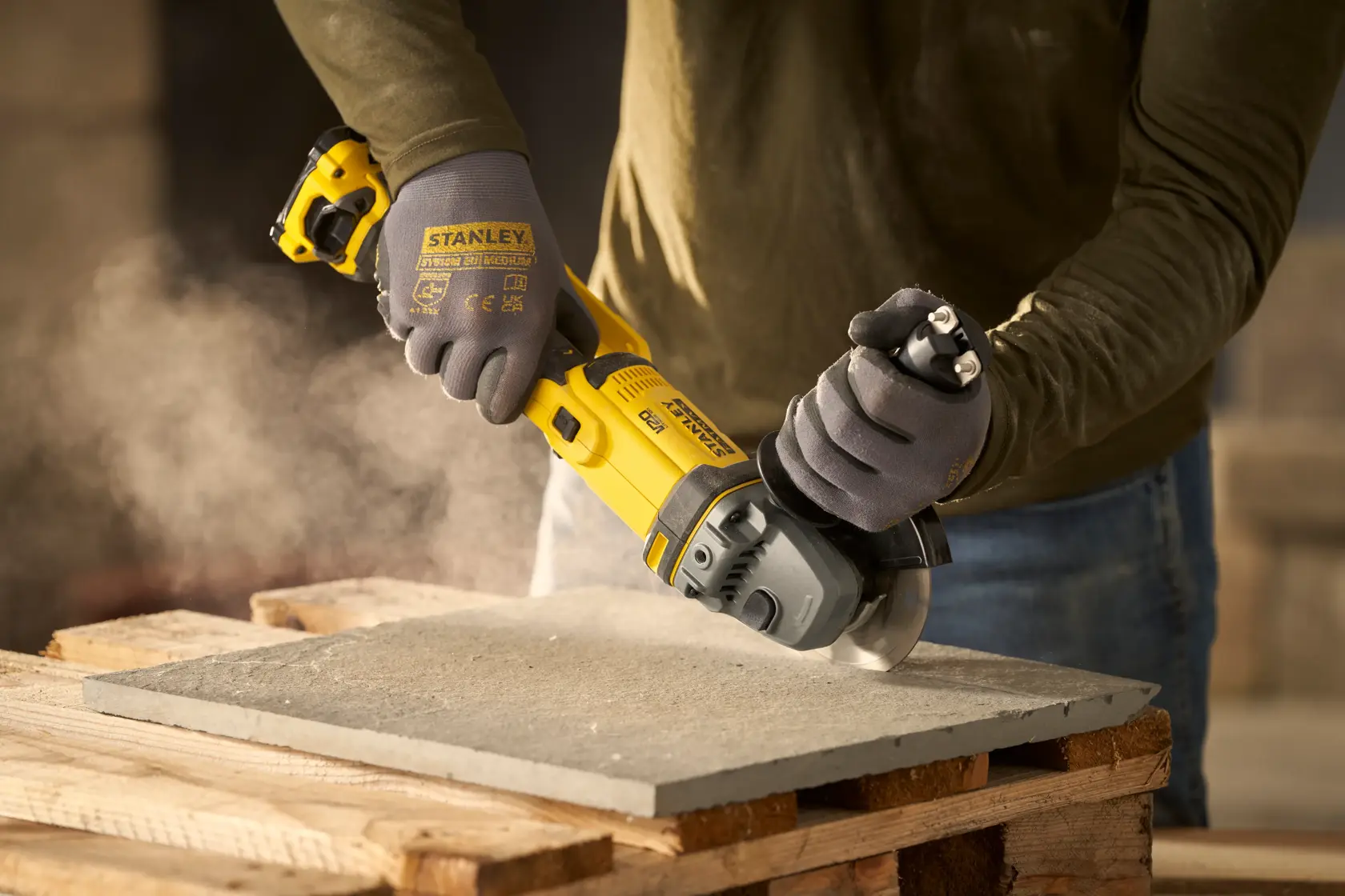 STANLEY SFMCG300B meuleuse d’angle en utilisation coupant une dalle de béton, gros plan sur mains gantées.