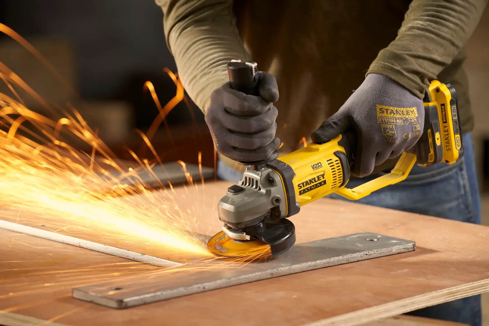 Photo de la meuleuse d’angle STANLEY SFMCG300B en action, meulant du métal avec des étincelles, l’utilisateur porte des gants.