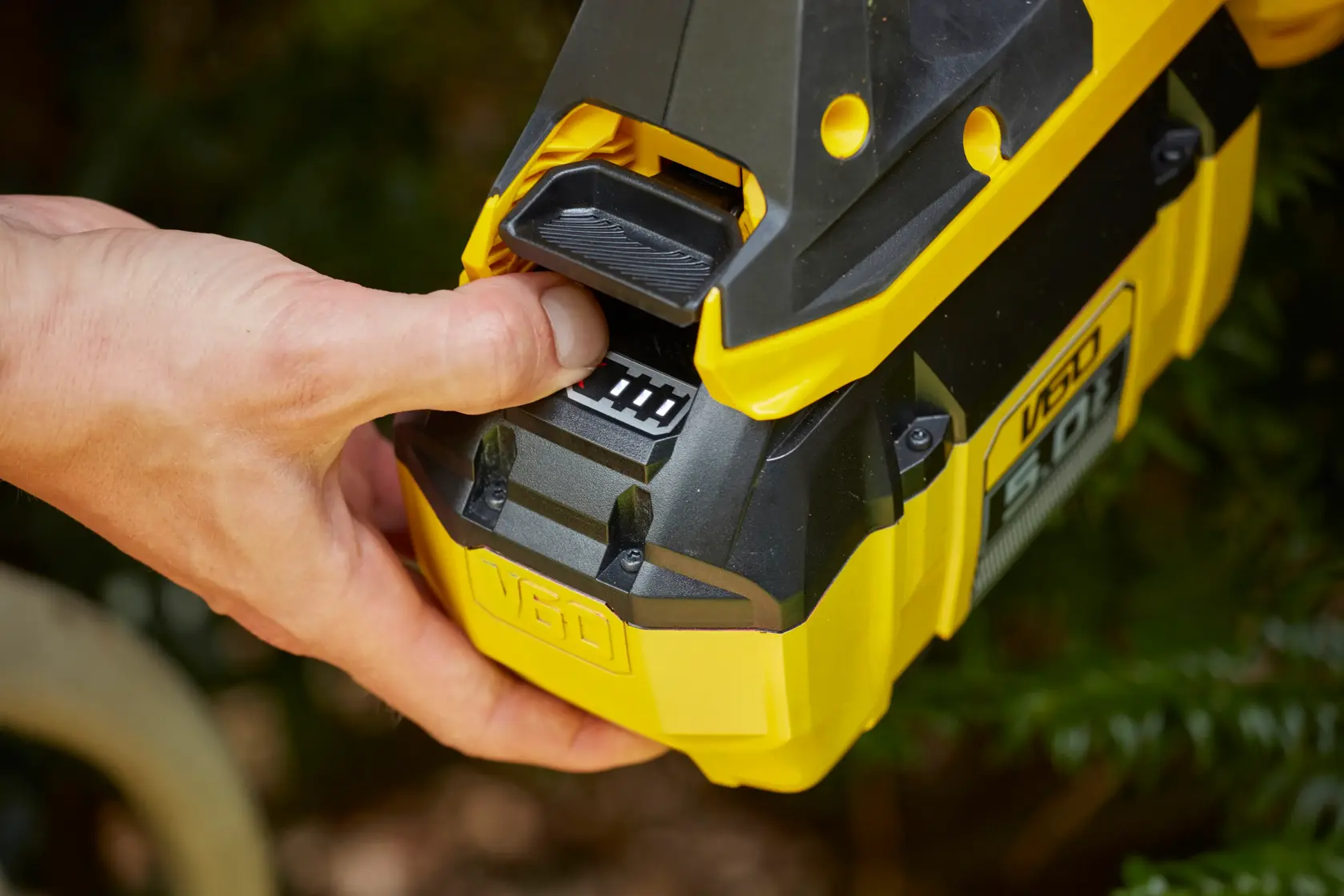 STANLEY SFMCHTB866B battery close-up with hand pressing release, yellow and black outdoor tool.