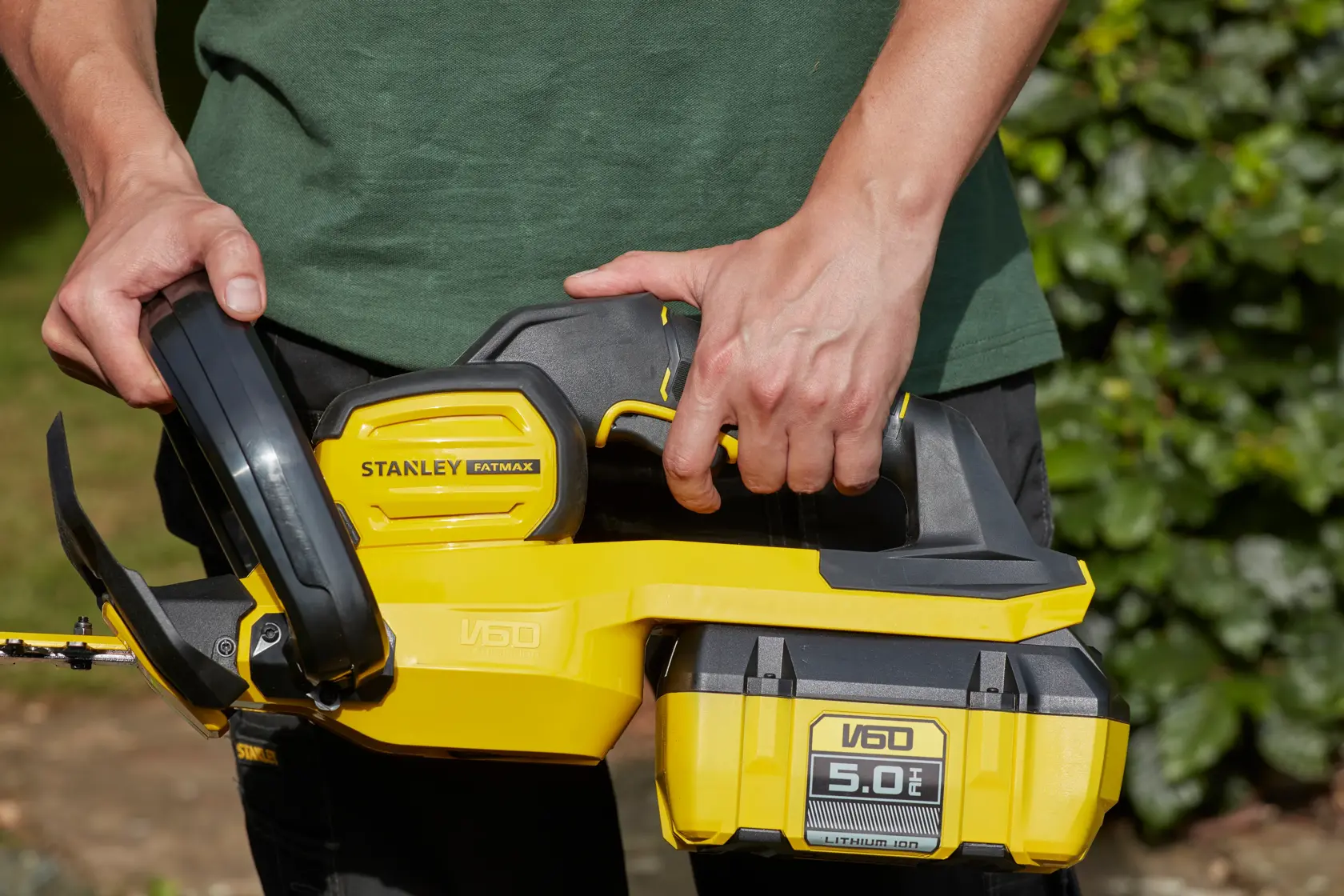 Photo of STANLEY SFMCHTB866B hedge trimmer, yellow and black, held by person outdoors.
