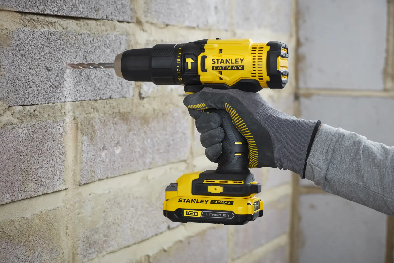 Perceuse-visseuse sans fil STANLEY SFMCK465D2S en cours d'utilisation perçant un mur en brique, vue rapprochée latérale.