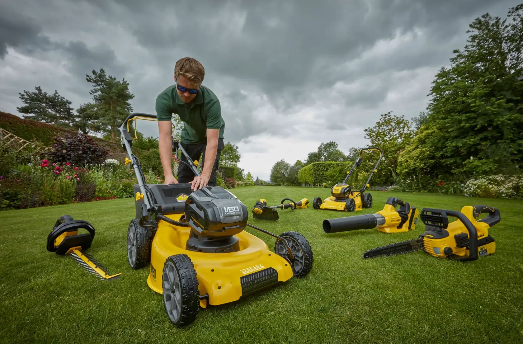 Photo de la tondeuse STANLEY SFMCMW2653B avec outils de jardin sans fil sur pelouse.