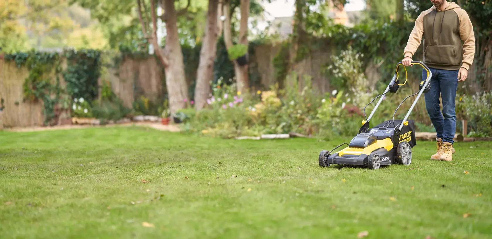 Photo of STANLEY SFMCMWS251M lawn mower in use on green grass, side angle, yellow and black design.