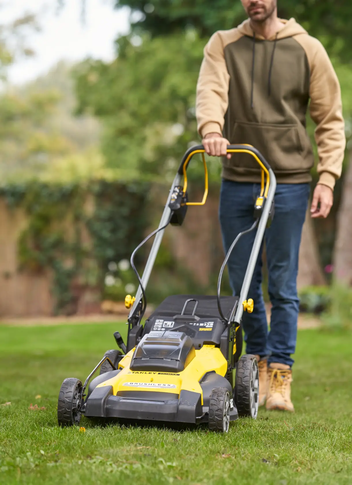 STANLEY SFMCMWS251M lawn mower with yellow and black body, shown in use on grass, front angle.