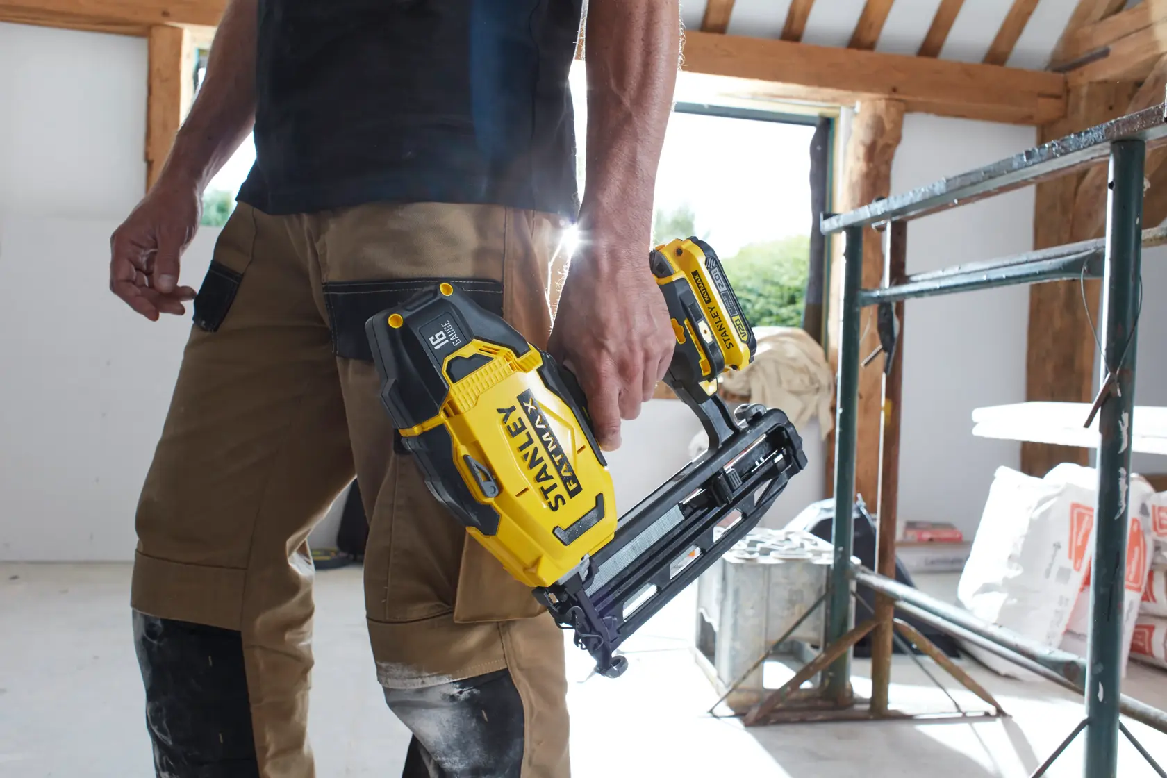 Cloueur sans fil STANLEY SFMCN616D2K tenu par une personne en pantalon de travail sur chantier.