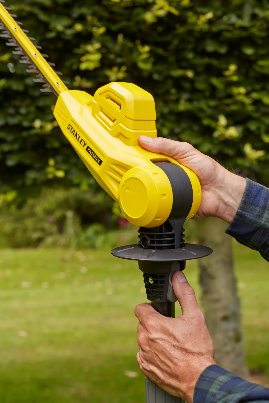 Fotografia del tagliasiepi a batteria giallo STANLEY SFMCPH845M1 tenuto in un giardino.