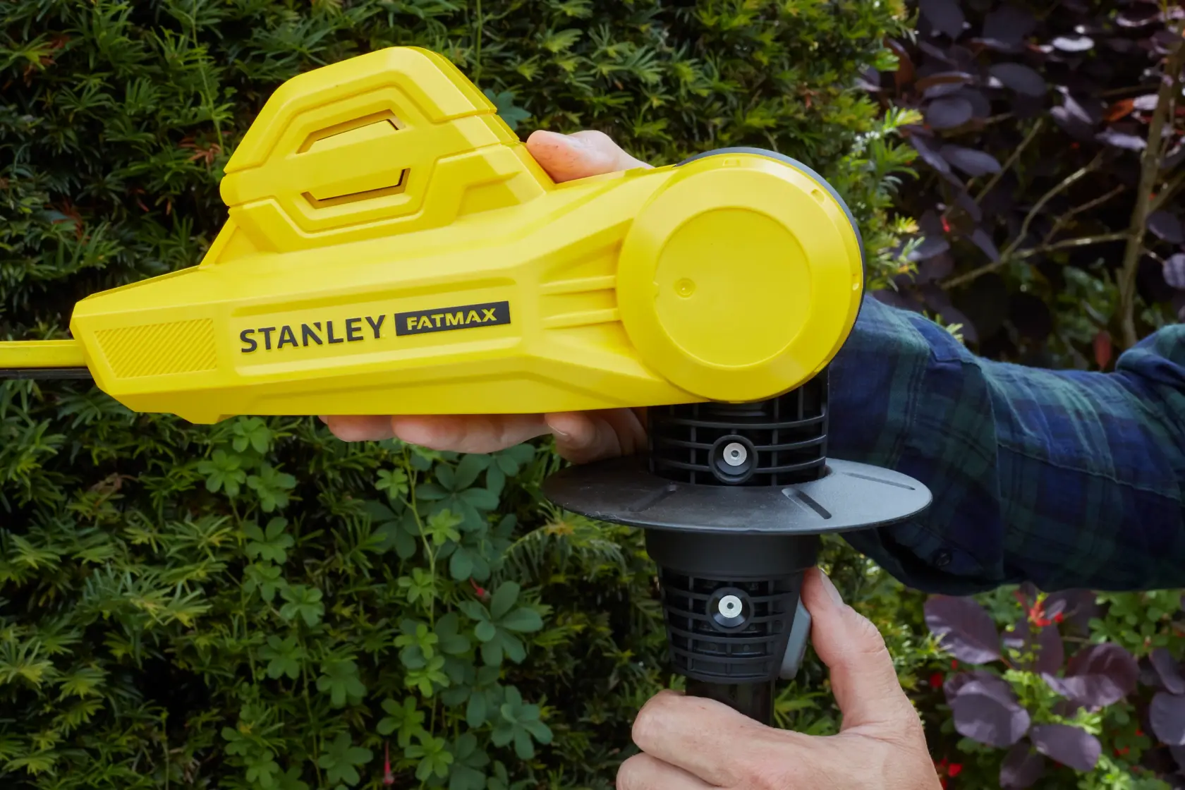 STANLEY SFMCPH845M1 tagliasiepi senza fili giallo in uso, primo piano dell'impugnatura e del corpo con sfondo da giardino.