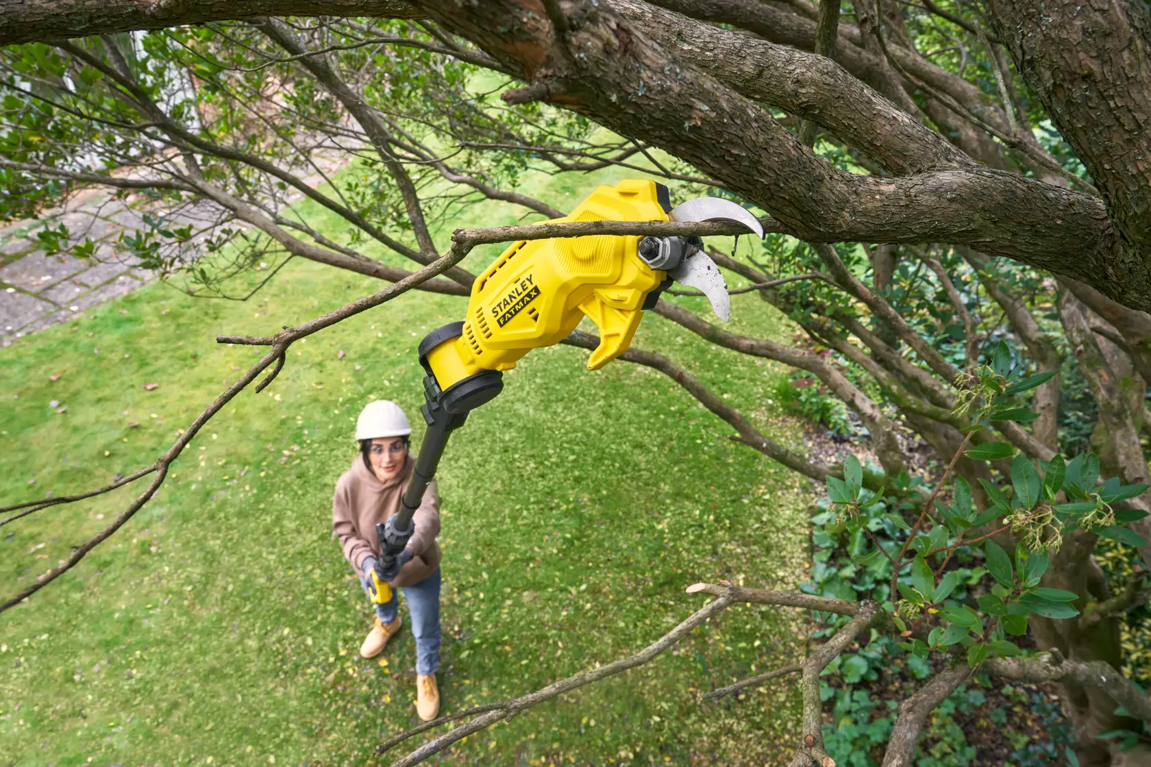 STANLEY SFMCPP632D1 potatore a batteria giallo su asta che taglia un ramo in un giardino esterno.