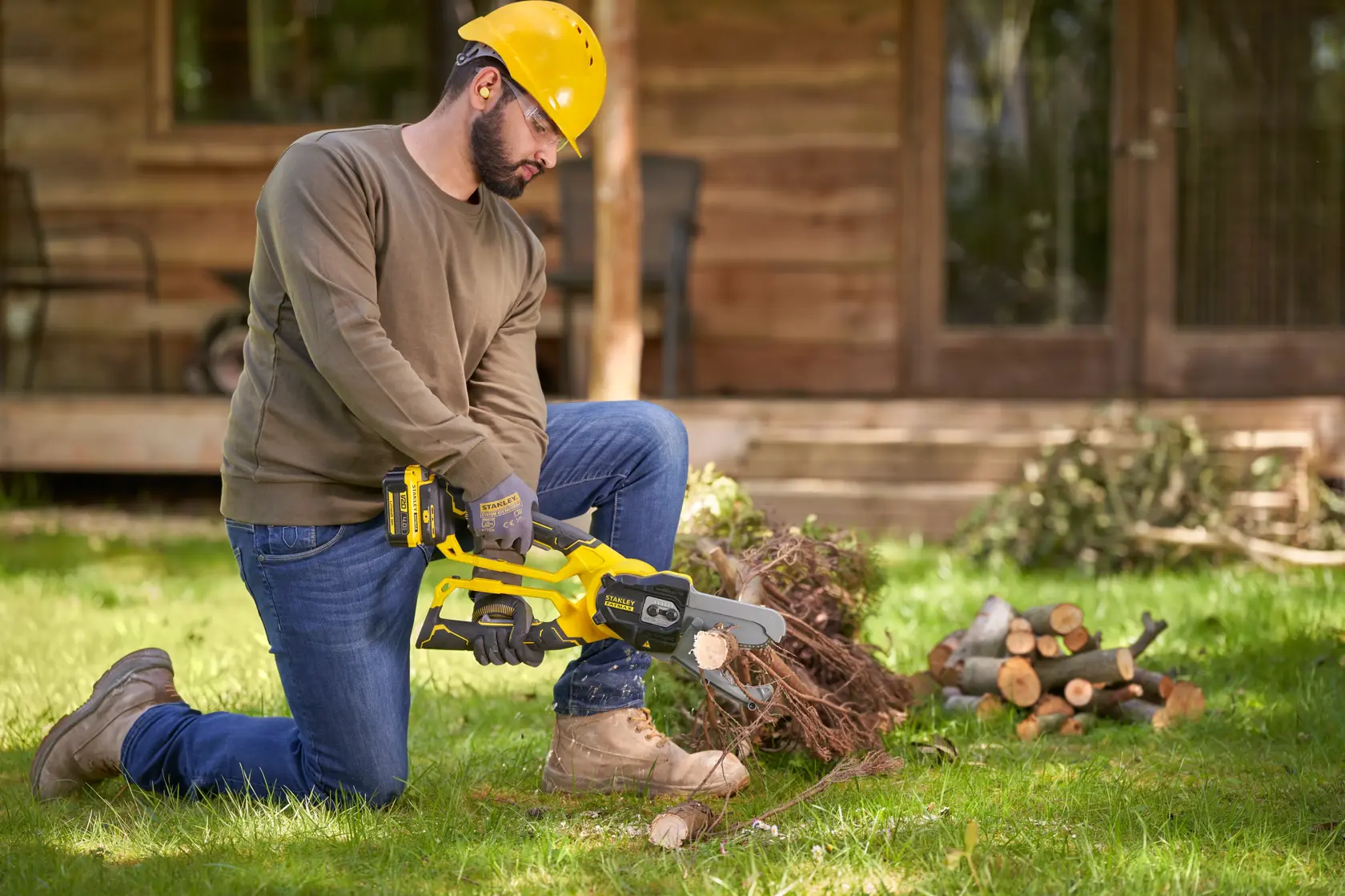 Photo of a person using a STANLEY SFMCPS515B cordless chainsaw to cut branches outdoors on grass.