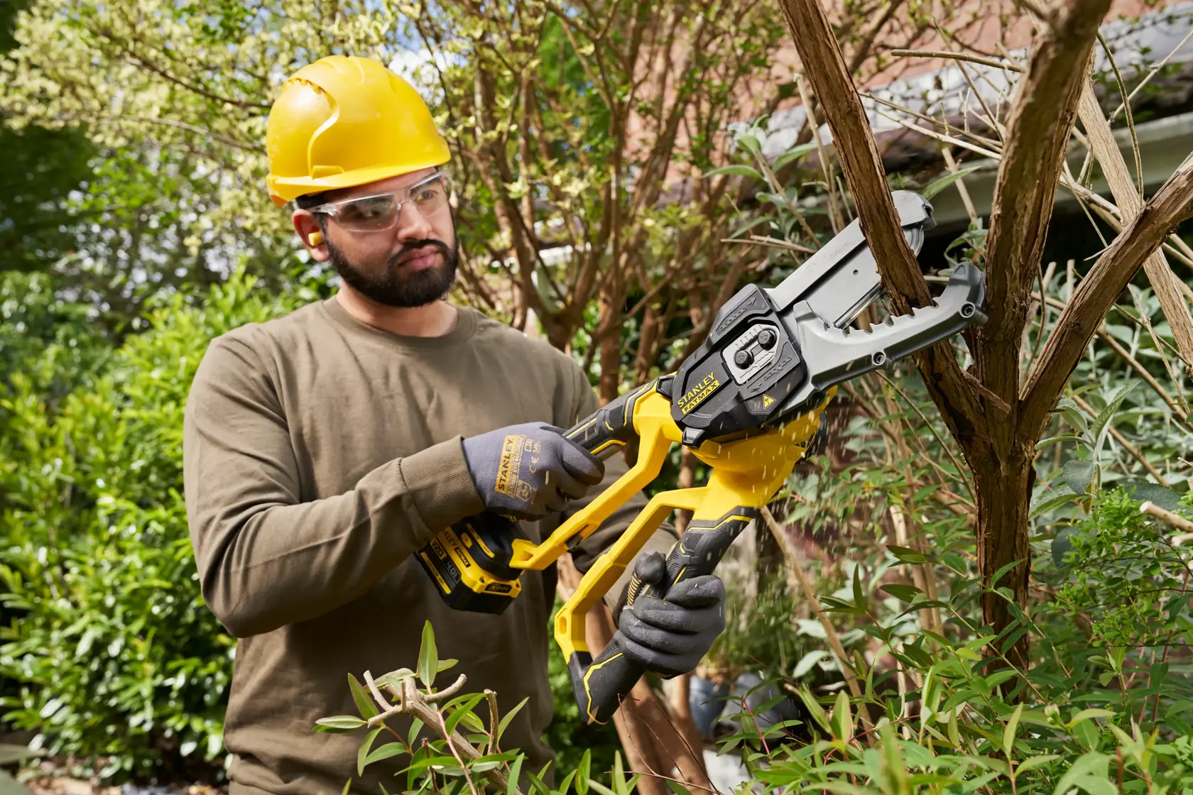 Foto di un operatore che usa la motosega a batteria STANLEY SFMCPS515M1 per tagliare rami in giardino.