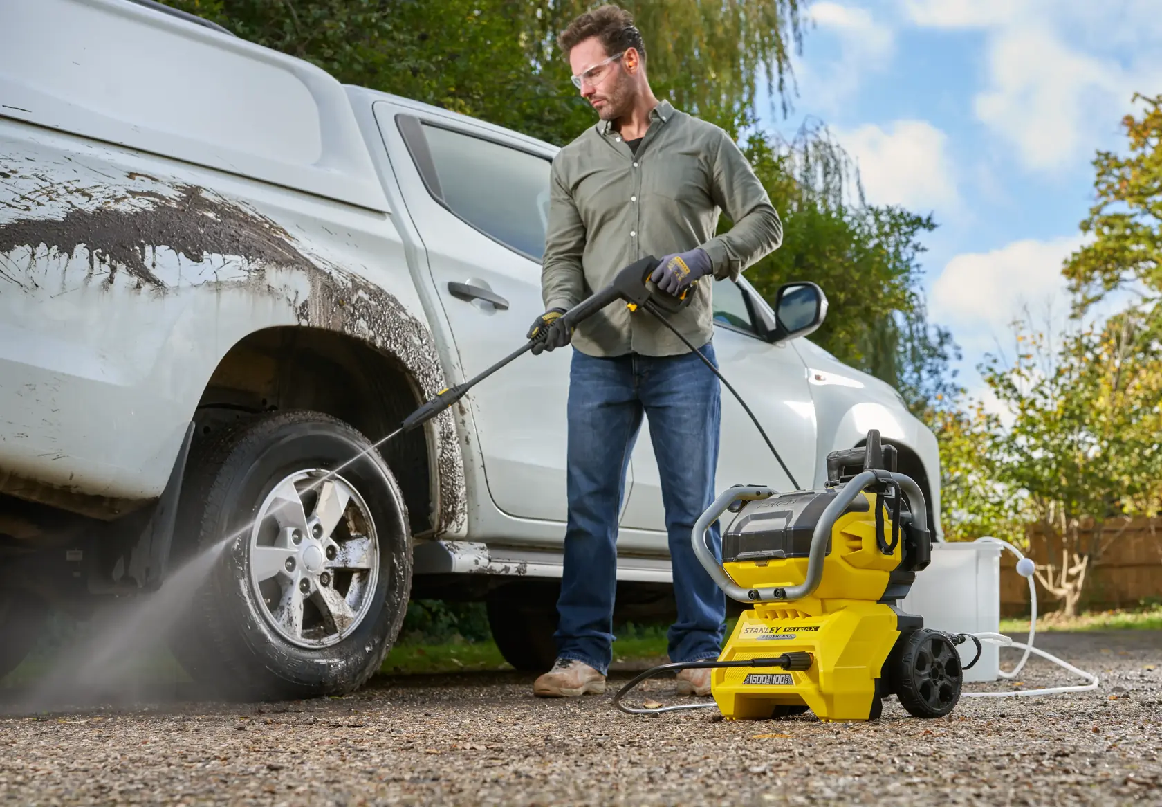 STANLEY SFMCPW1500B pressure washer used outdoors to clean muddy truck, with hose connected and water spraying.