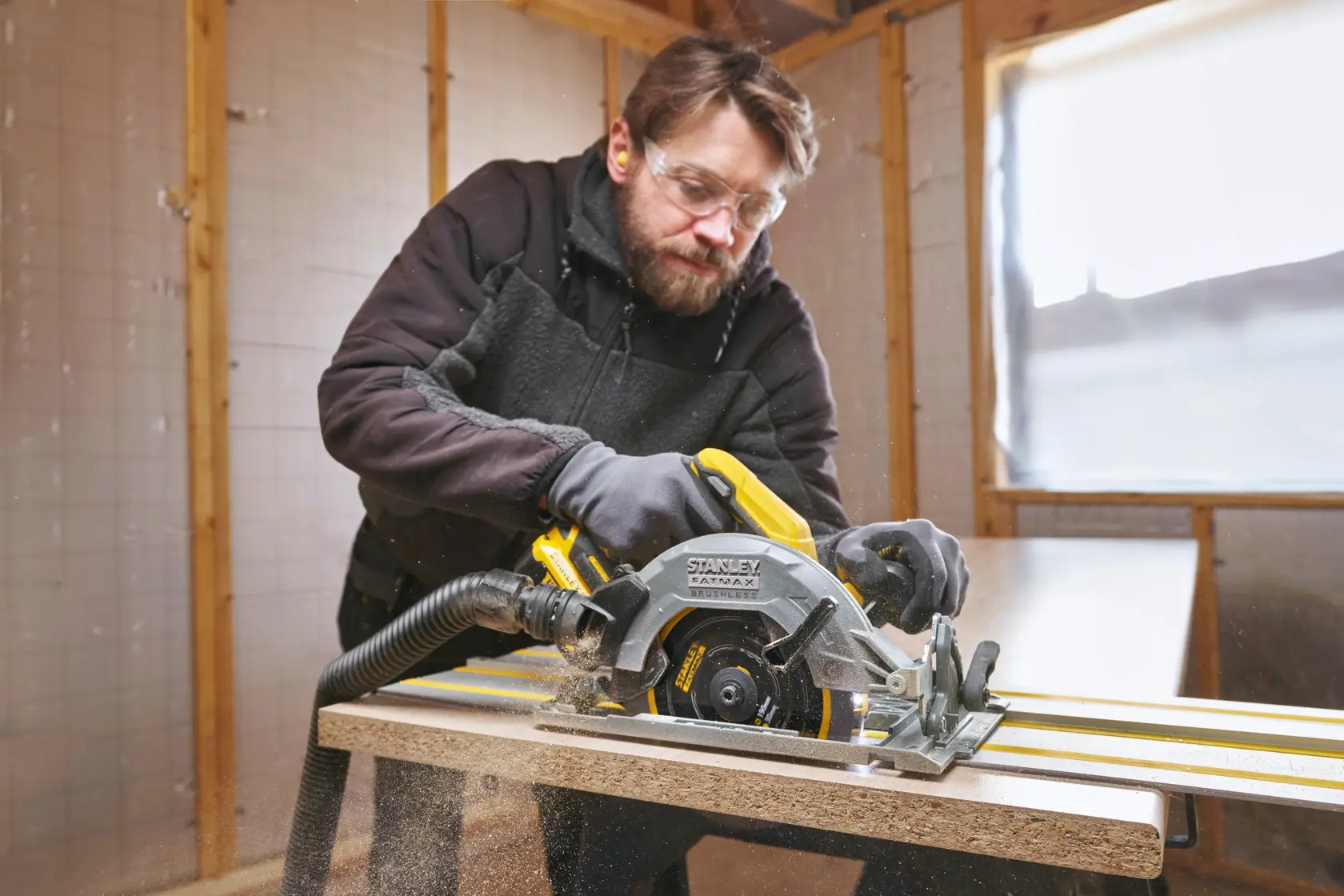 Photo of STANLEY SFMCS551B circular saw in use cutting wood, with dust extraction hose attached, inside workshop.