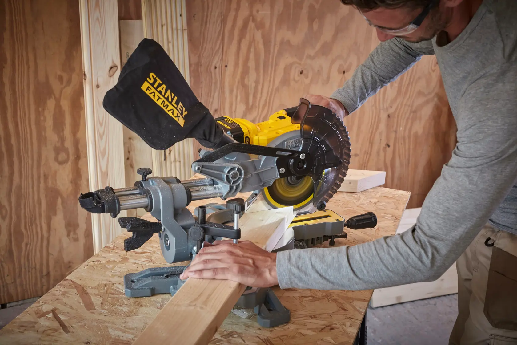 STANLEY SFMCS701M1 miter saw in use cutting wood on a workbench, dust bag attached, indoor construction setting.