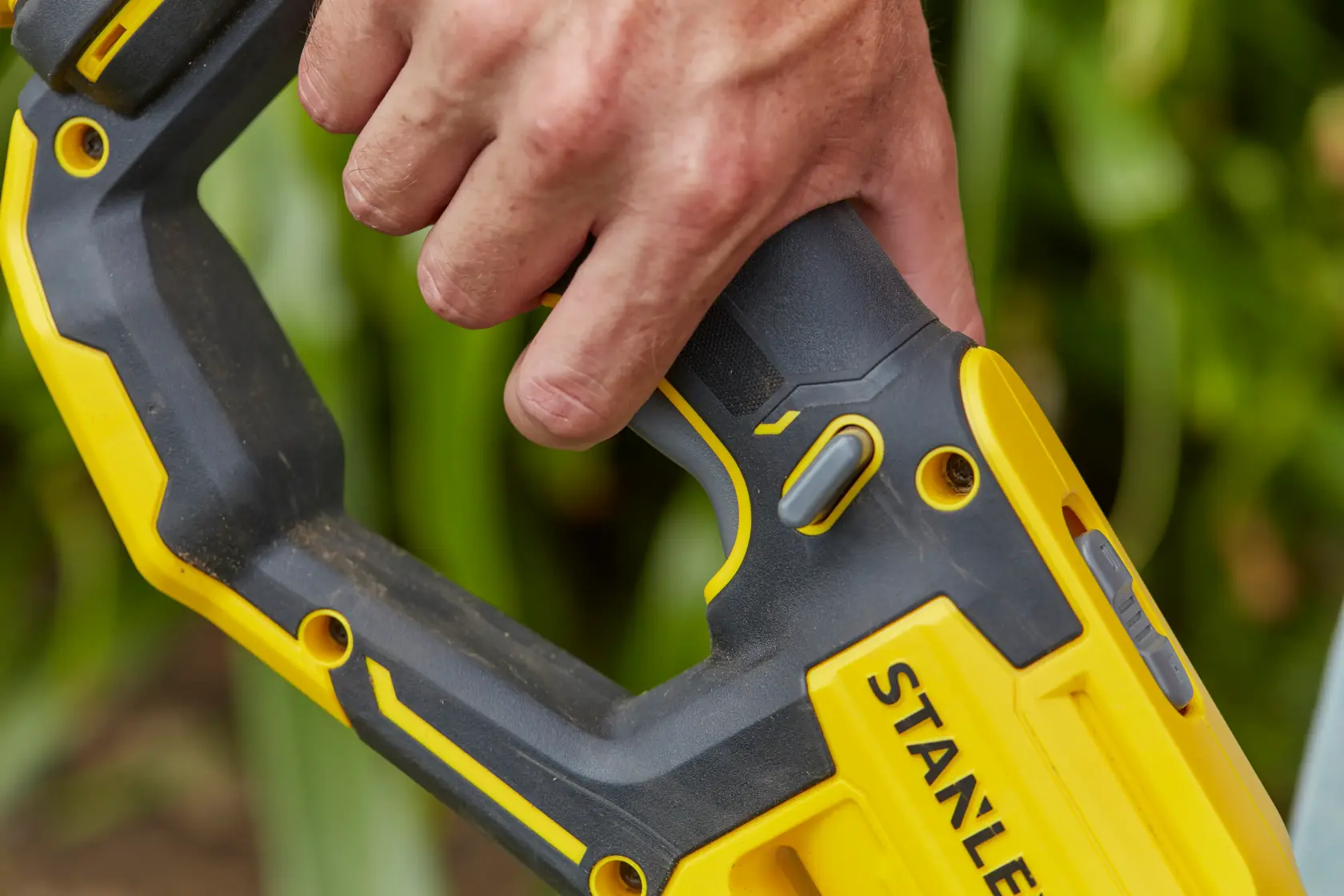 Photo of STANLEY SFMCST933B power tool handle in yellow and black, close-up with hand holding grip.
