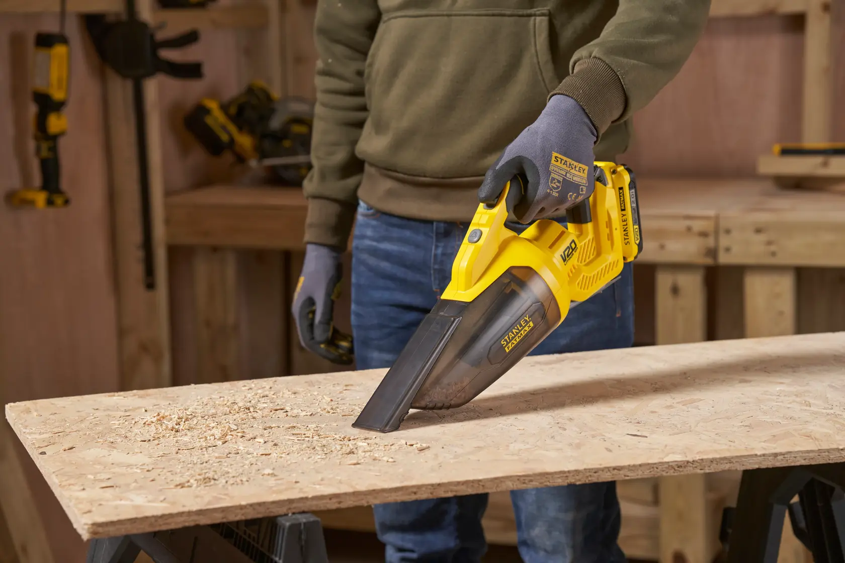 Aspirateur à main STANLEY SFMCVH001B utilisé sur une surface en bois, corps jaune, bac à poussière transparent.