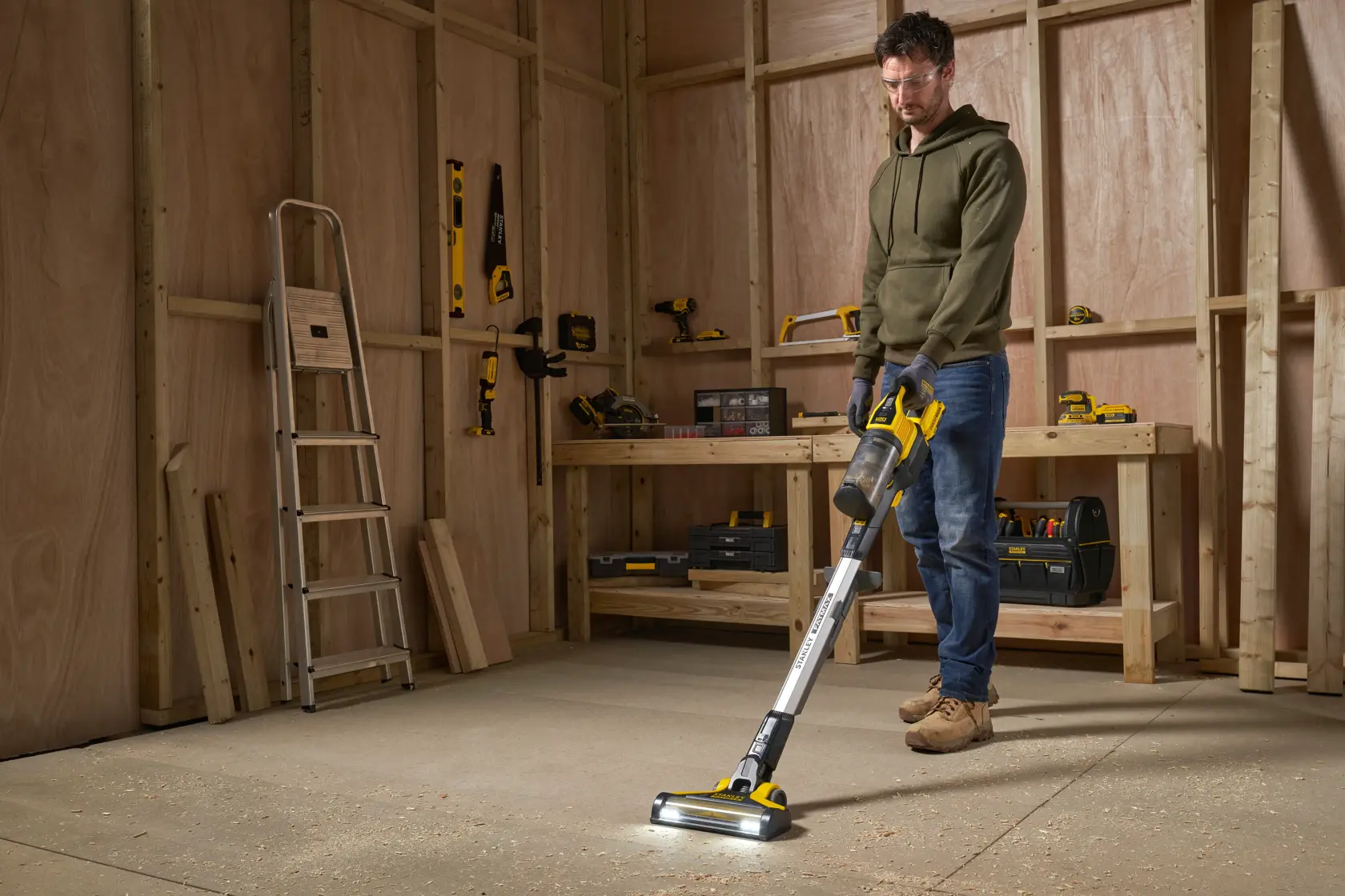 Aspirateur balai sans fil STANLEY SFMCVS001D1 en atelier, nettoyant la sciure au sol.