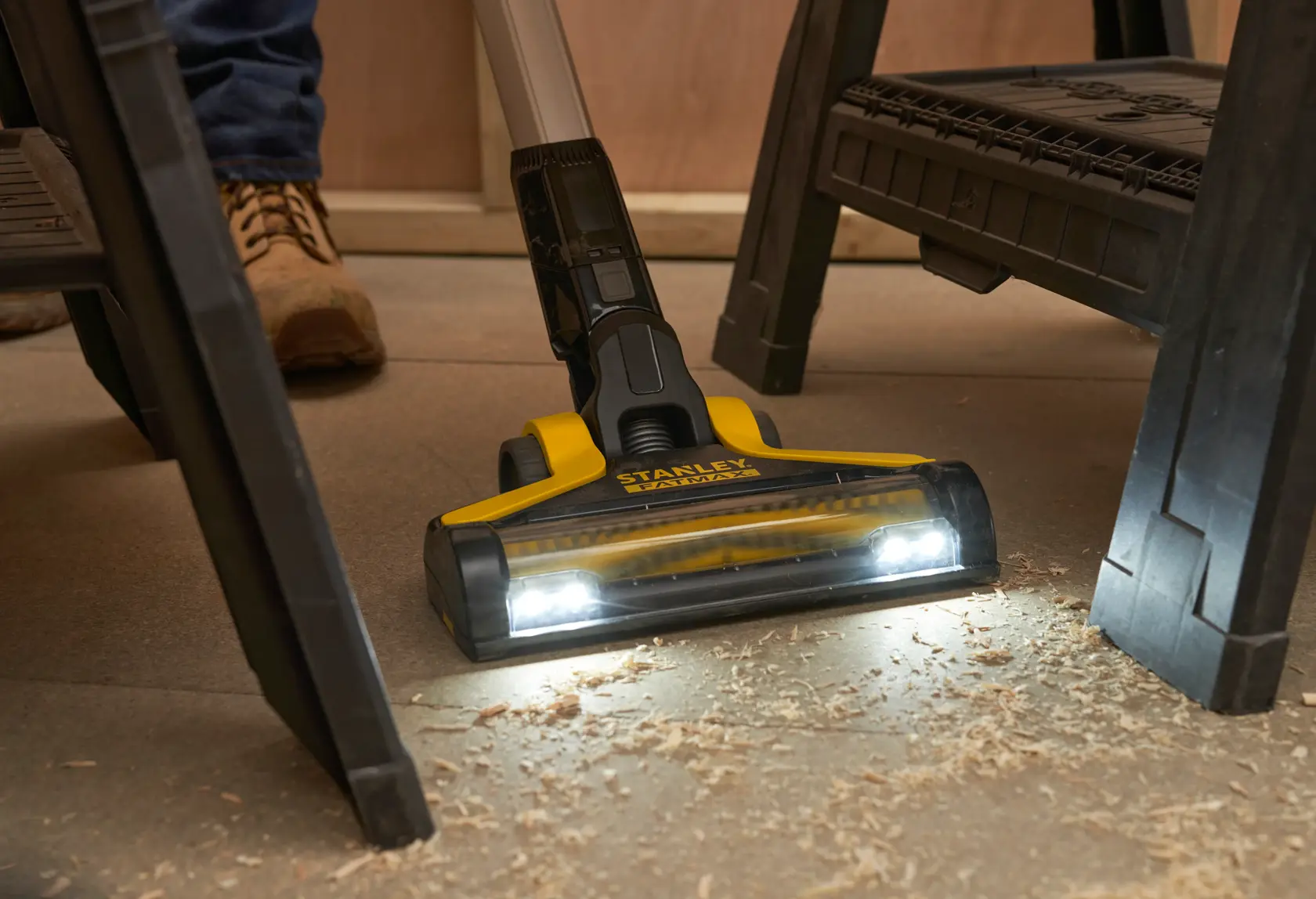STANLEY SFMCVS001D1 scopa elettrica senza fili con luci LED pulisce trucioli di legno sotto un banco da lavoro, vista frontale.
