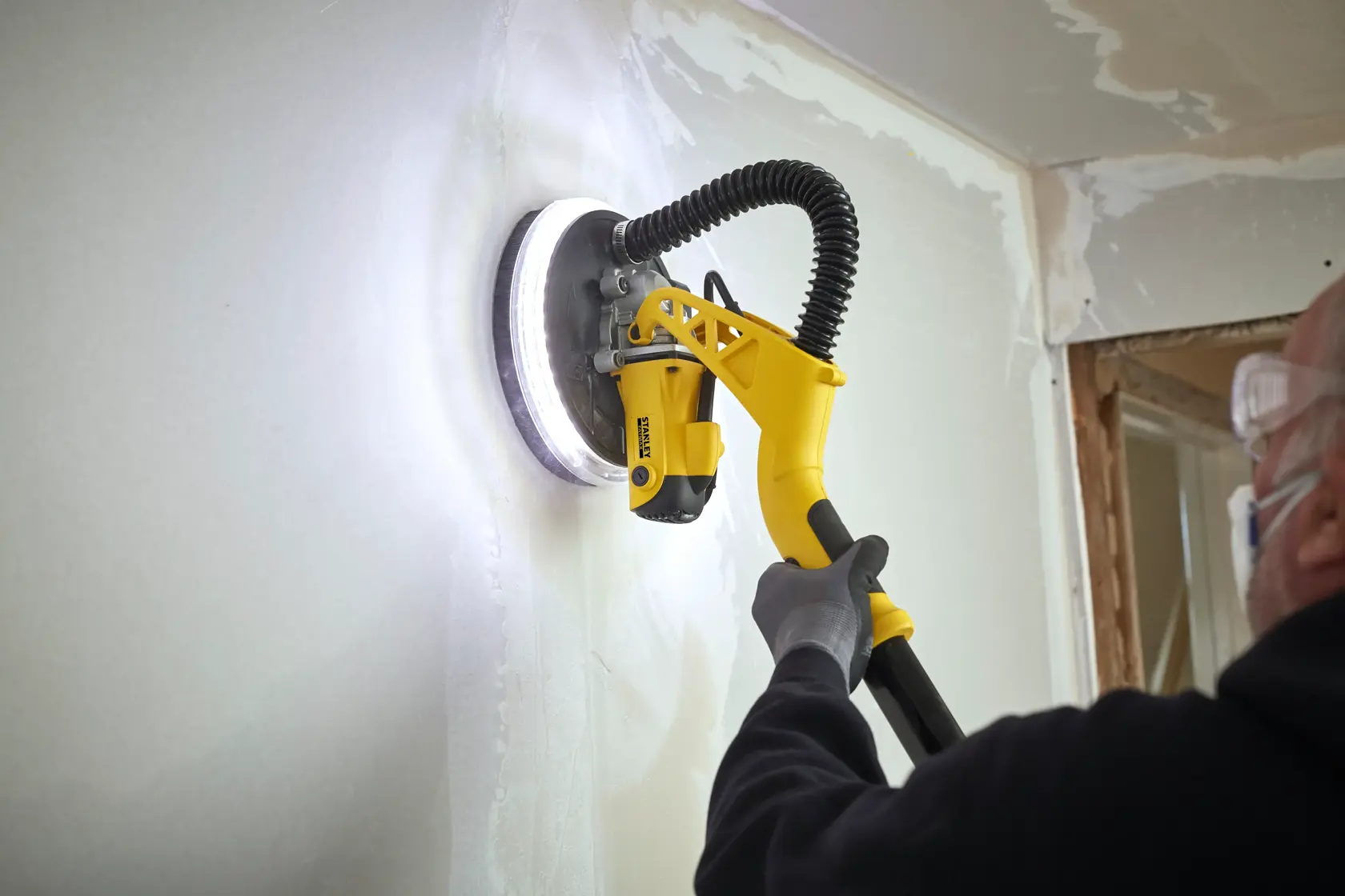 STANLEY SFMEE500S drywall sander in use, yellow handle, sanding white wall, close-up action.