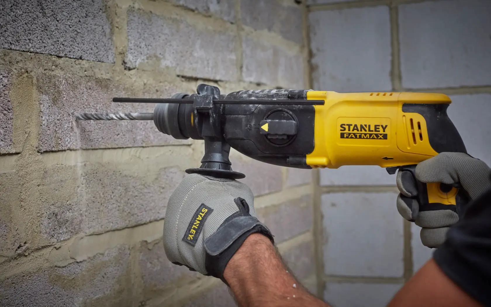 Foto des STANLEY SFMEH210K-QS Bohrhammers im Einsatz an einer Ziegelwand, gelb-schwarzes Design.