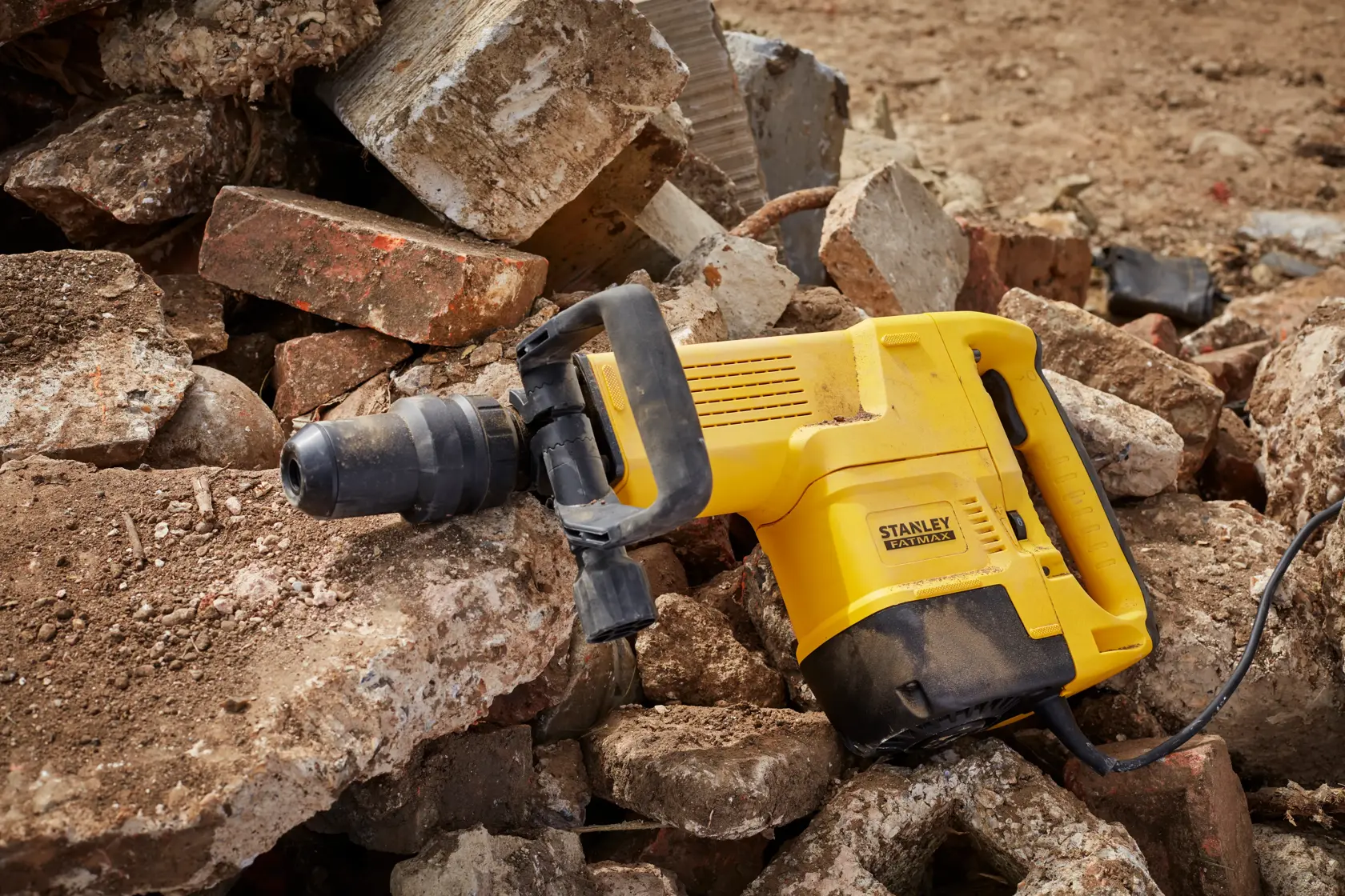 STANLEY SFMEH230K-QS demolition hammer resting on rubble, yellow body with black handle, side view.