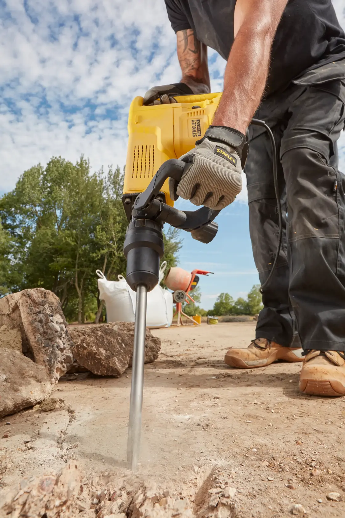 STANLEY SFMEH230K-QS demolition hammer in use breaking concrete outdoors, close-up on tool and worker’s hands.