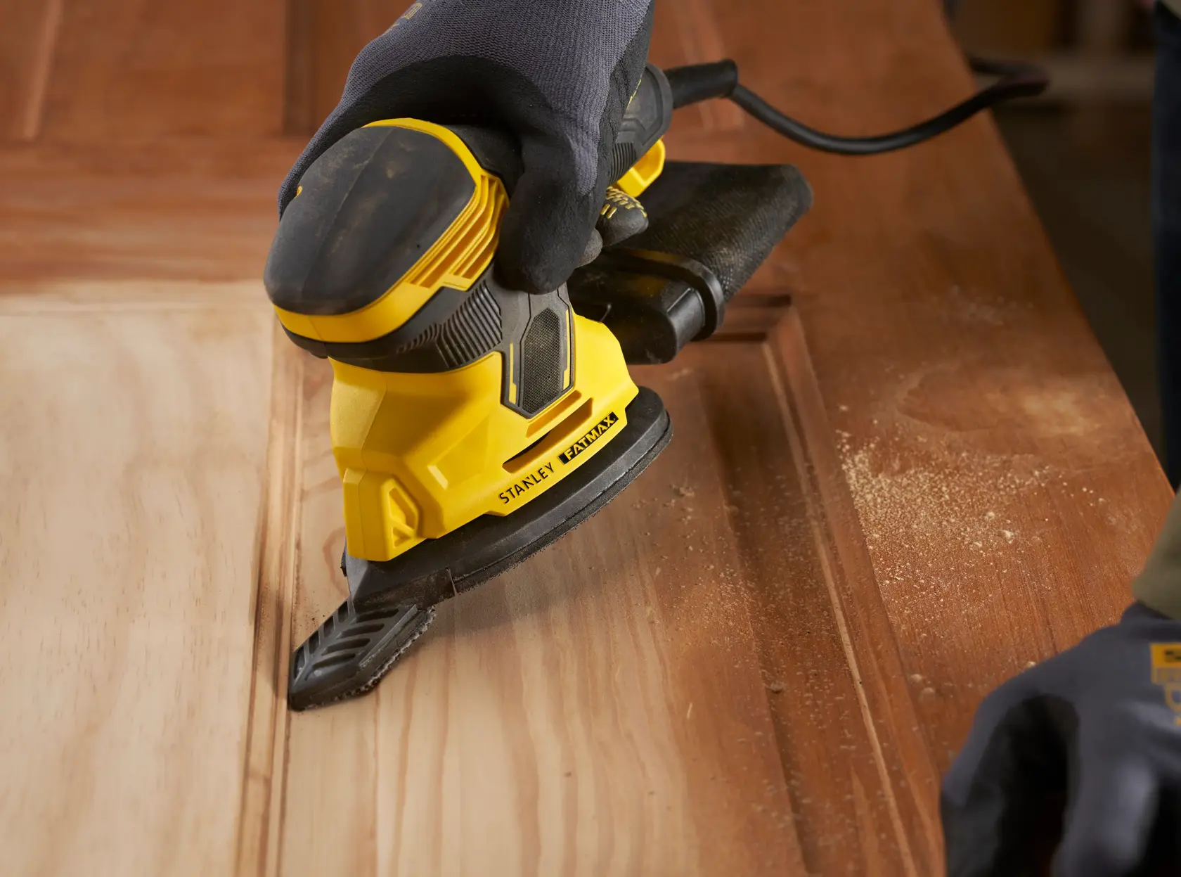 Fotografia della levigatrice STANLEY SFMEW210S in uso su superficie di legno, primo piano con polvere e design ergonomico.