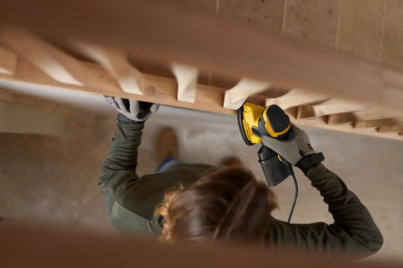 Persona che usa la levigatrice STANLEY SFMEW210S su corrimano in legno, vista dall'alto.