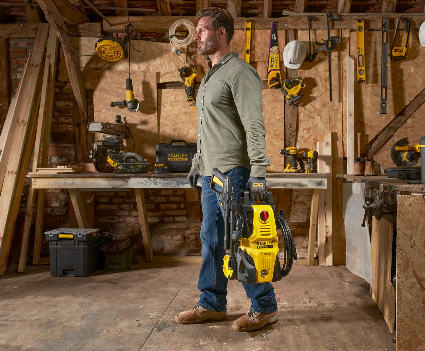 Stanley SFMPW1740 nettoyeur haute pression tenu par une personne dans un atelier avec outils de menuiserie.