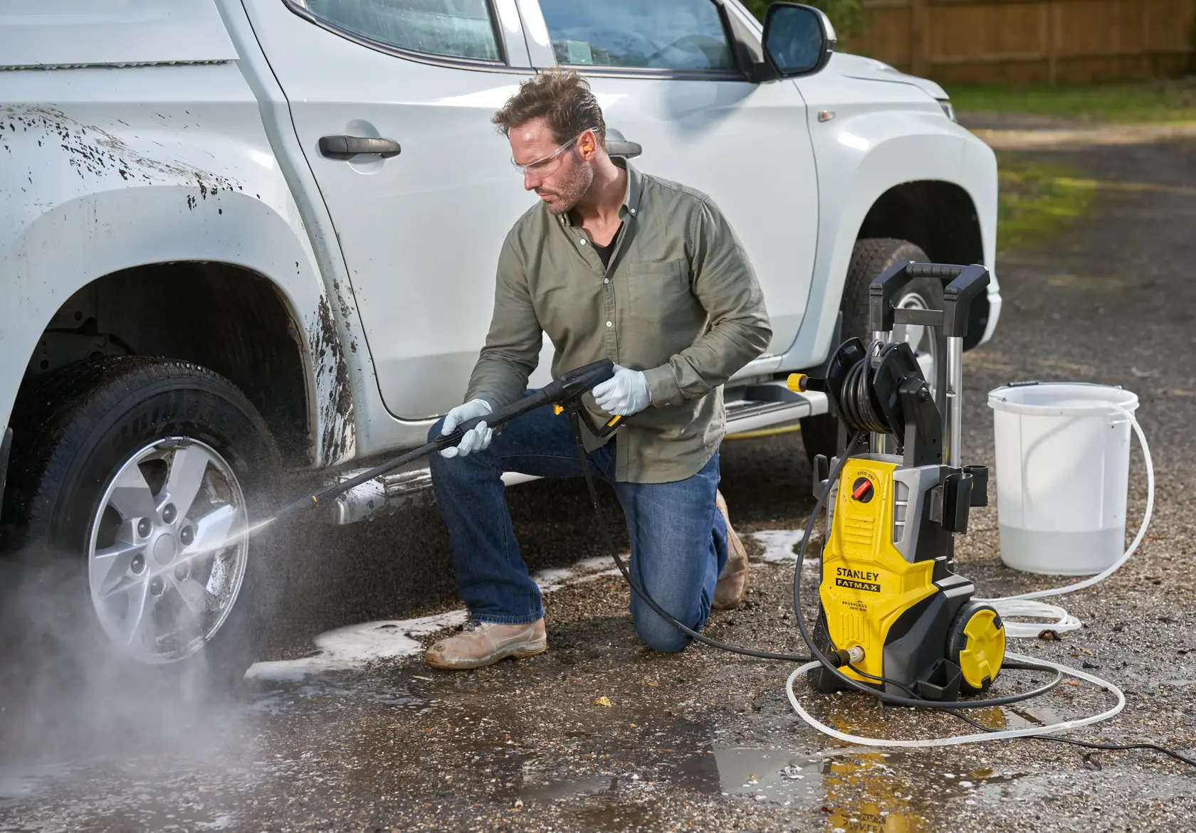 Stanley SFMPW2400 nettoyeur haute pression nettoyant une roue de voiture; unité jaune, tuyau, seau extérieur.