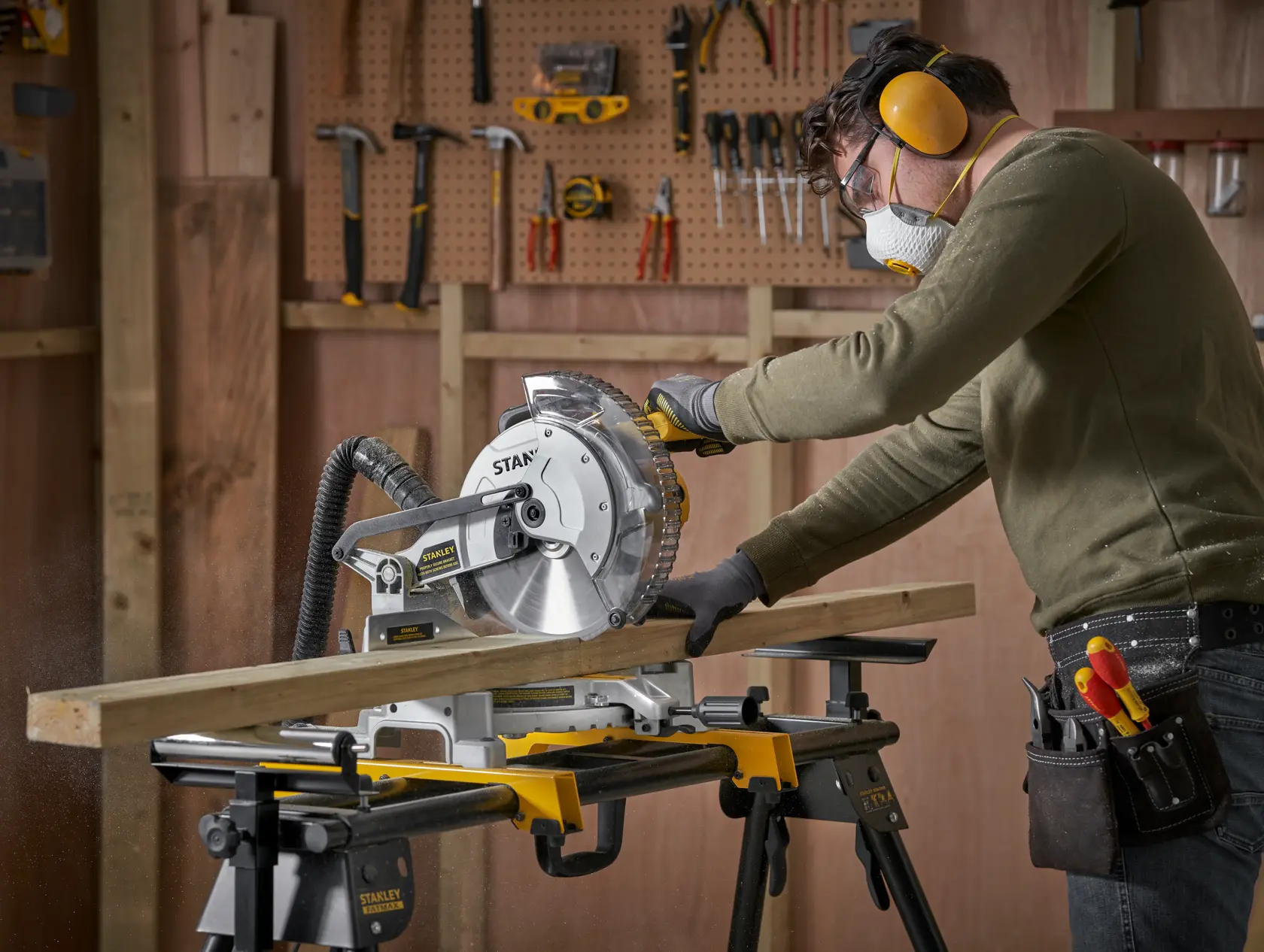 Foto di una persona che utilizza la troncatrice STANLEY SM1650 per tagliare legno in un laboratorio con utensili a parete.