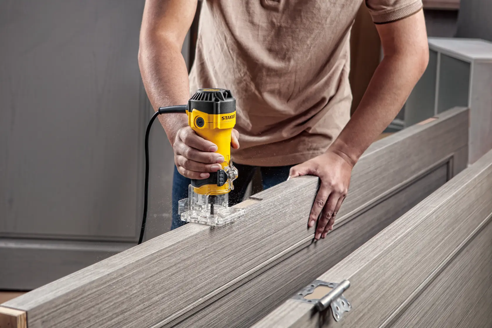 Photo de la défonceuse compacte STANLEY ST55-B2 utilisée sur une porte en bois, base transparente, utilisateur tenant l’outil d’une main.