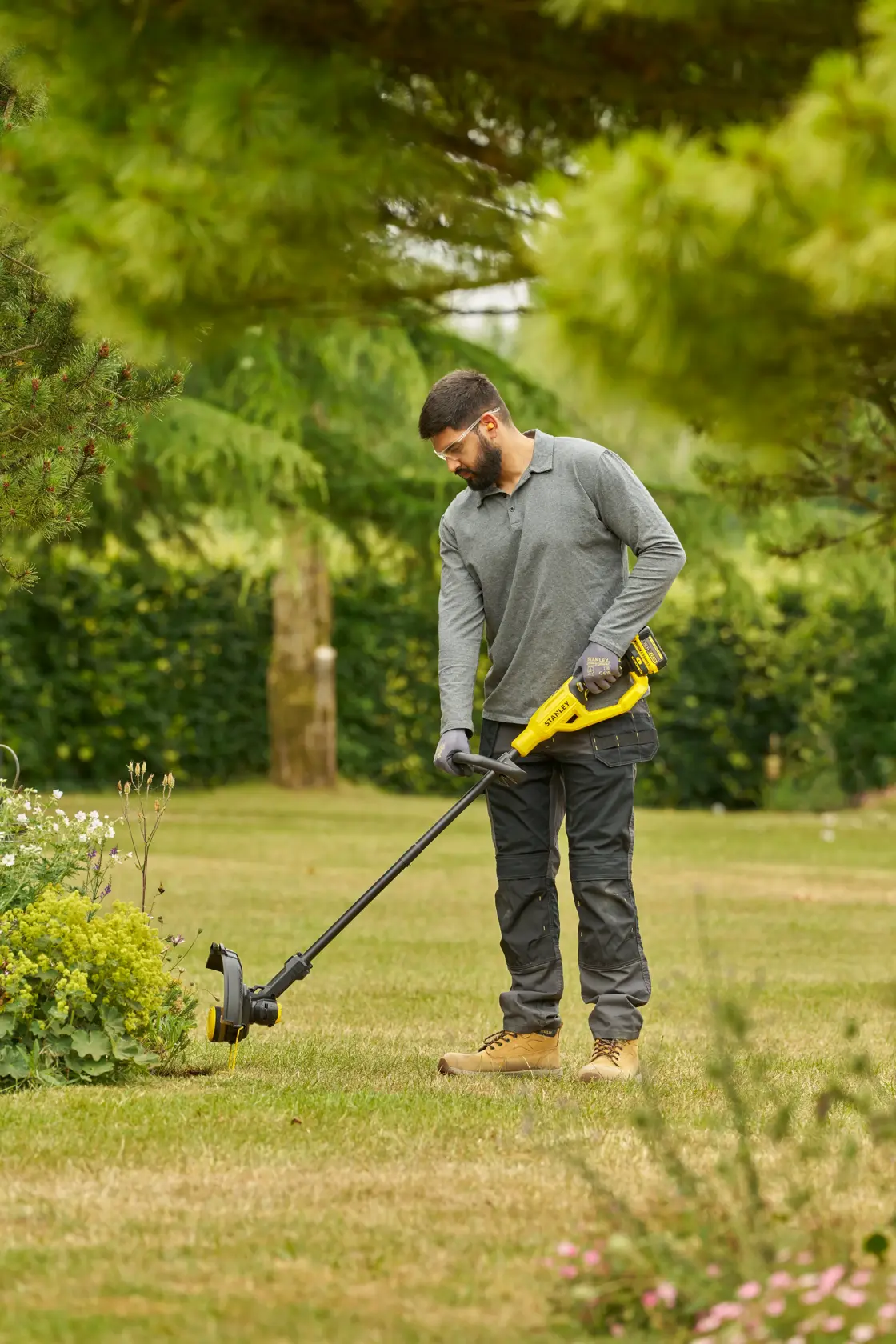 Coupe-bordures STANLEY STCST933M1 utilisé en extérieur dans un jardin, design jaune et noir, sur batterie.