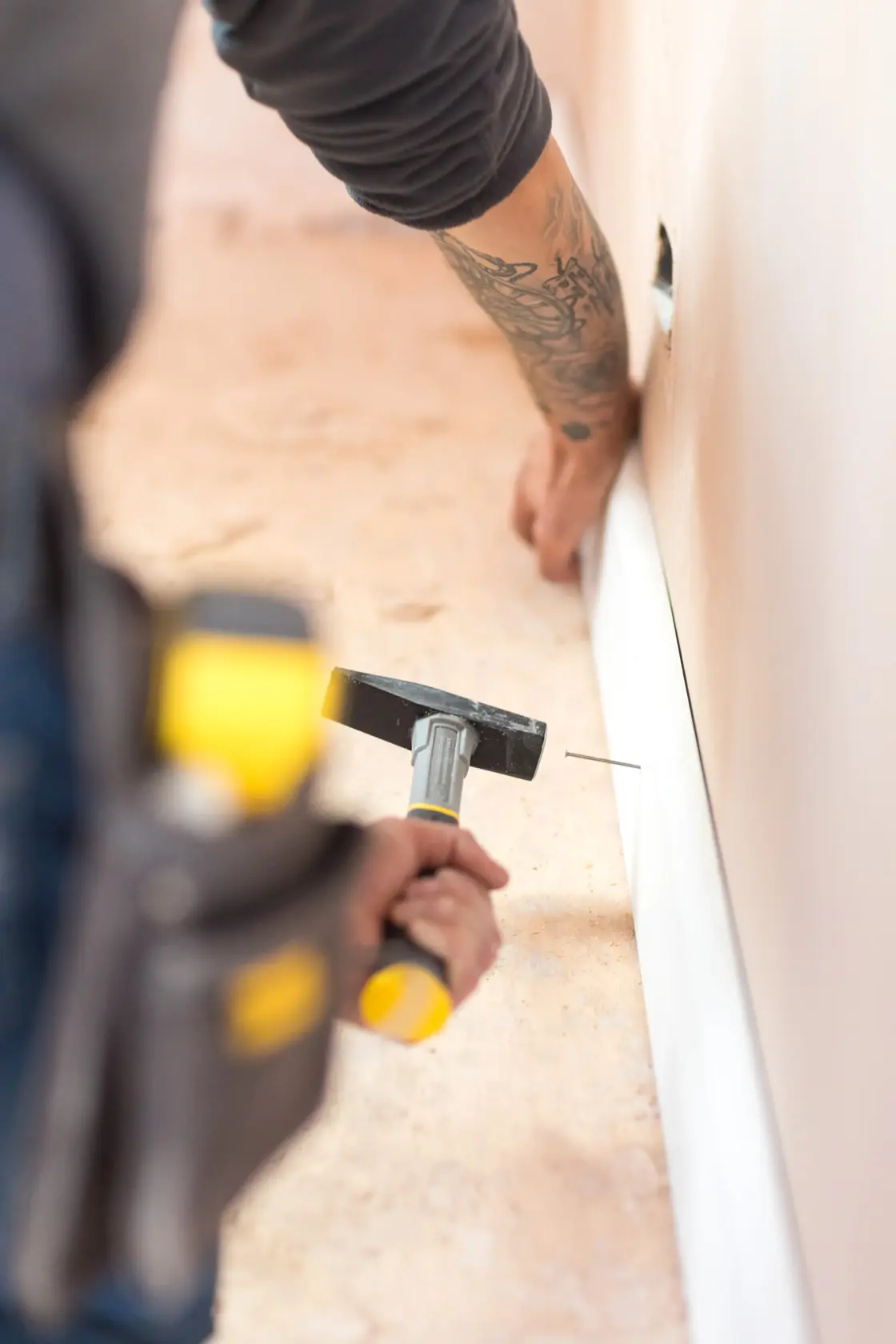 STANLEY STHT0-51908 Hammer im Einsatz, Person nagelt Sockelleiste an die Wand, seitliche Nahaufnahme.