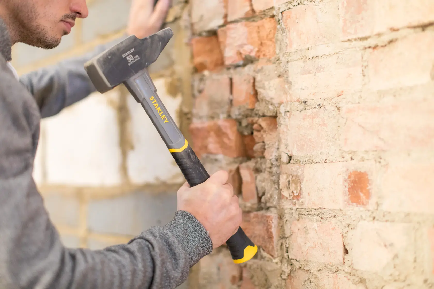 Stanley STHT0-54157 hammer with black and yellow handle used on a brick wall, side angle.