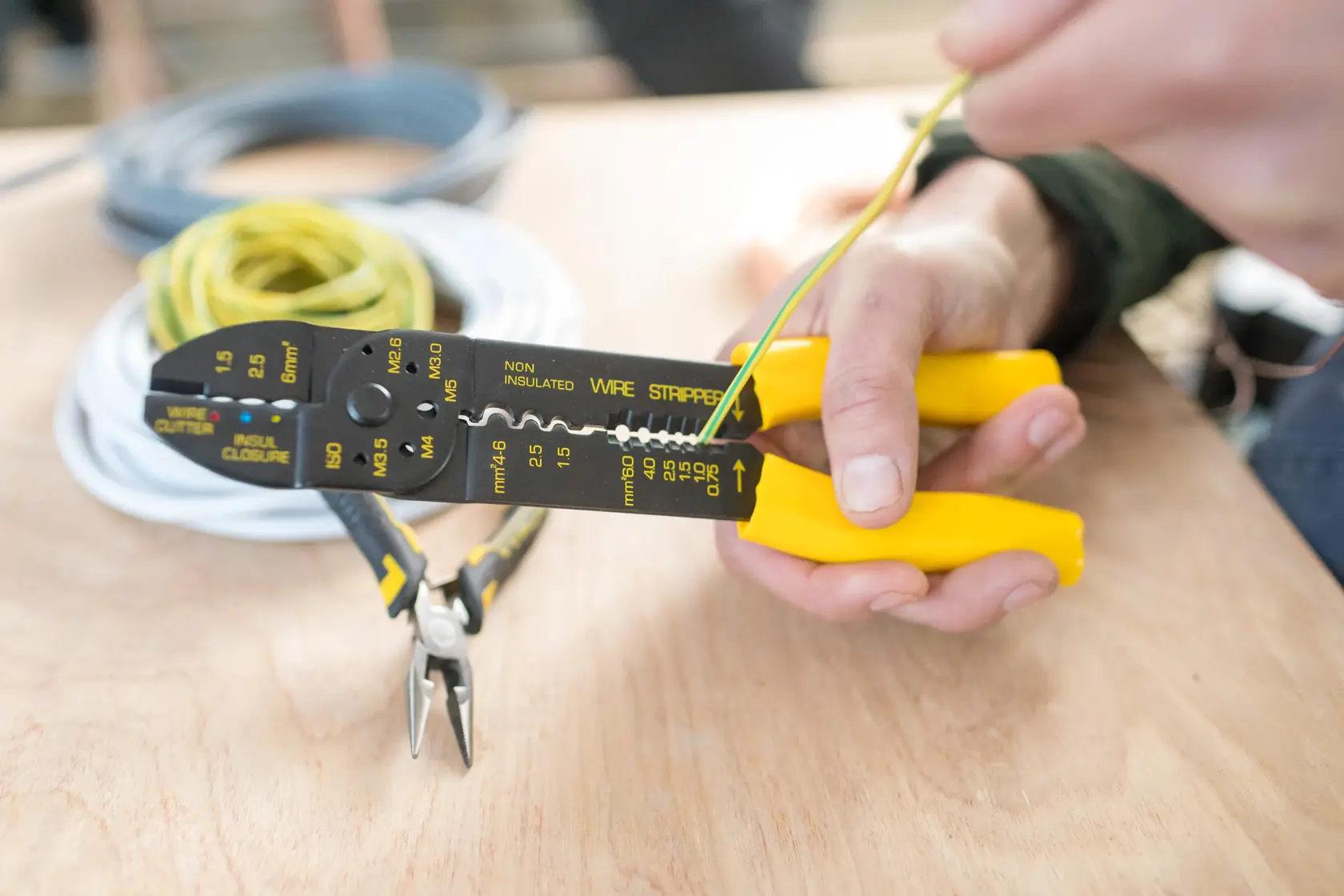 Photo of STANLEY STHT0-75414 wire stripper with yellow handles stripping wire on a workbench.