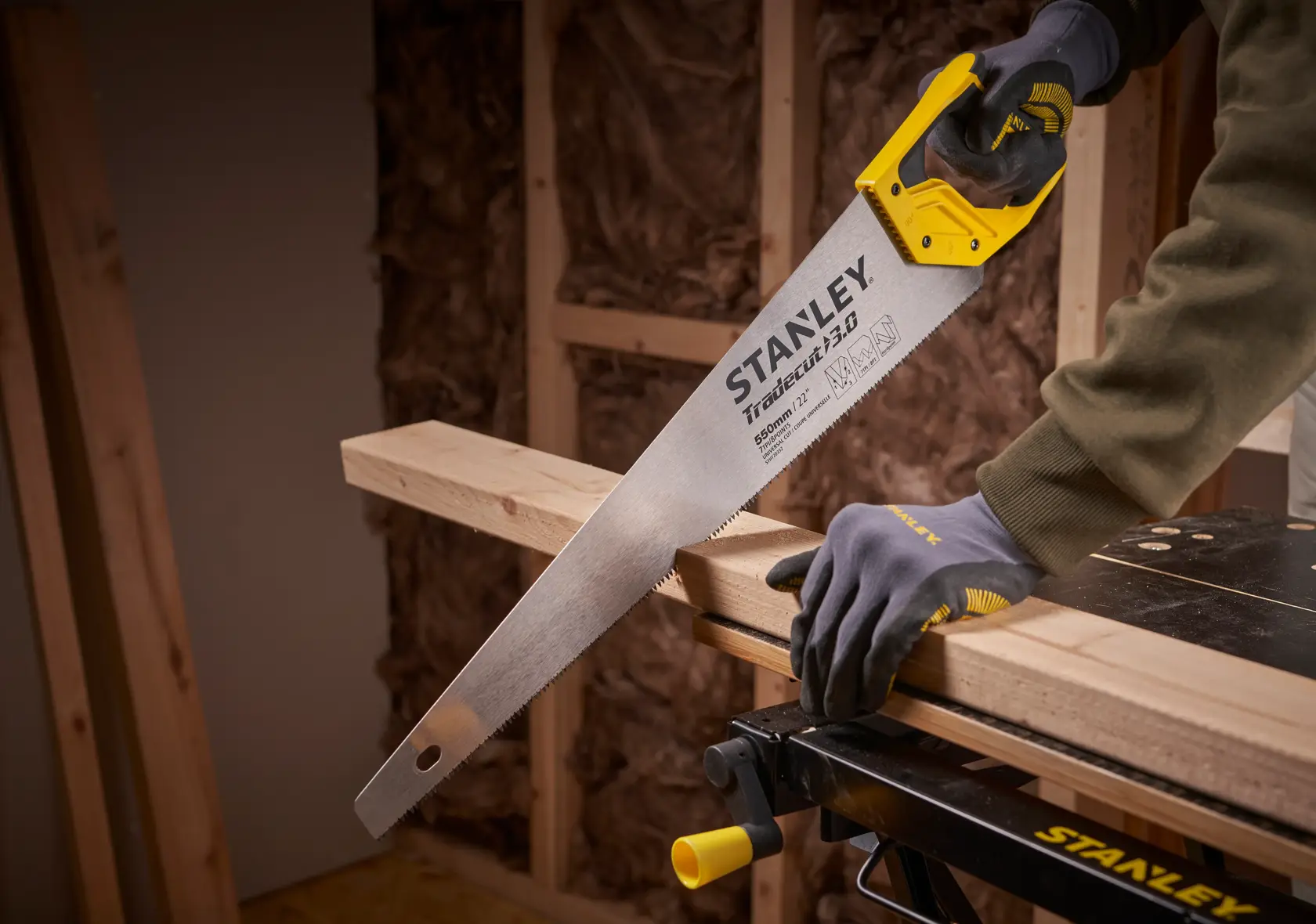 STANLEY STHT1-20352 scie à main à poignée jaune coupant une poutre en bois dans un atelier.