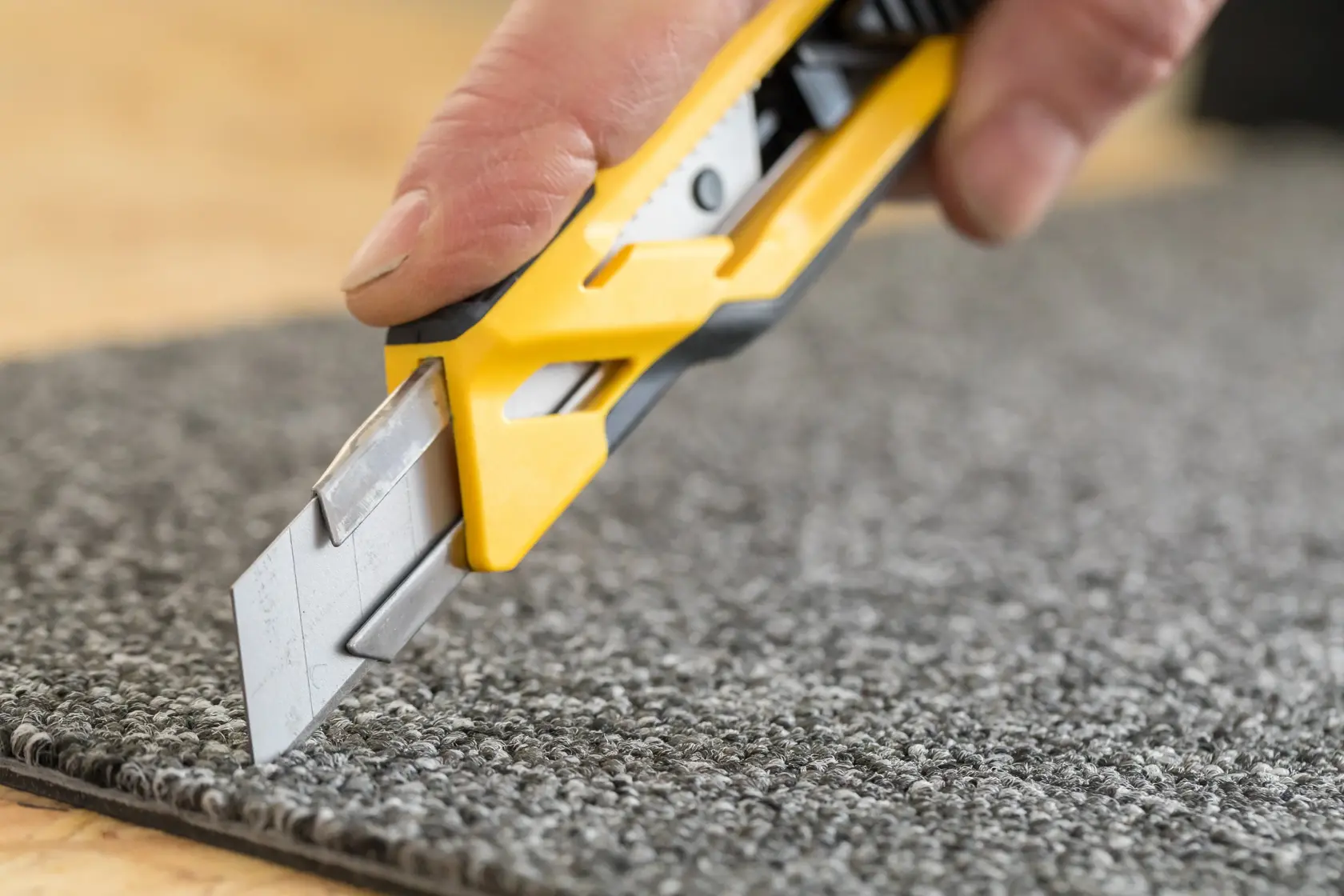Gros plan d'une main utilisant un cutter jaune pour couper un tapis gris.
