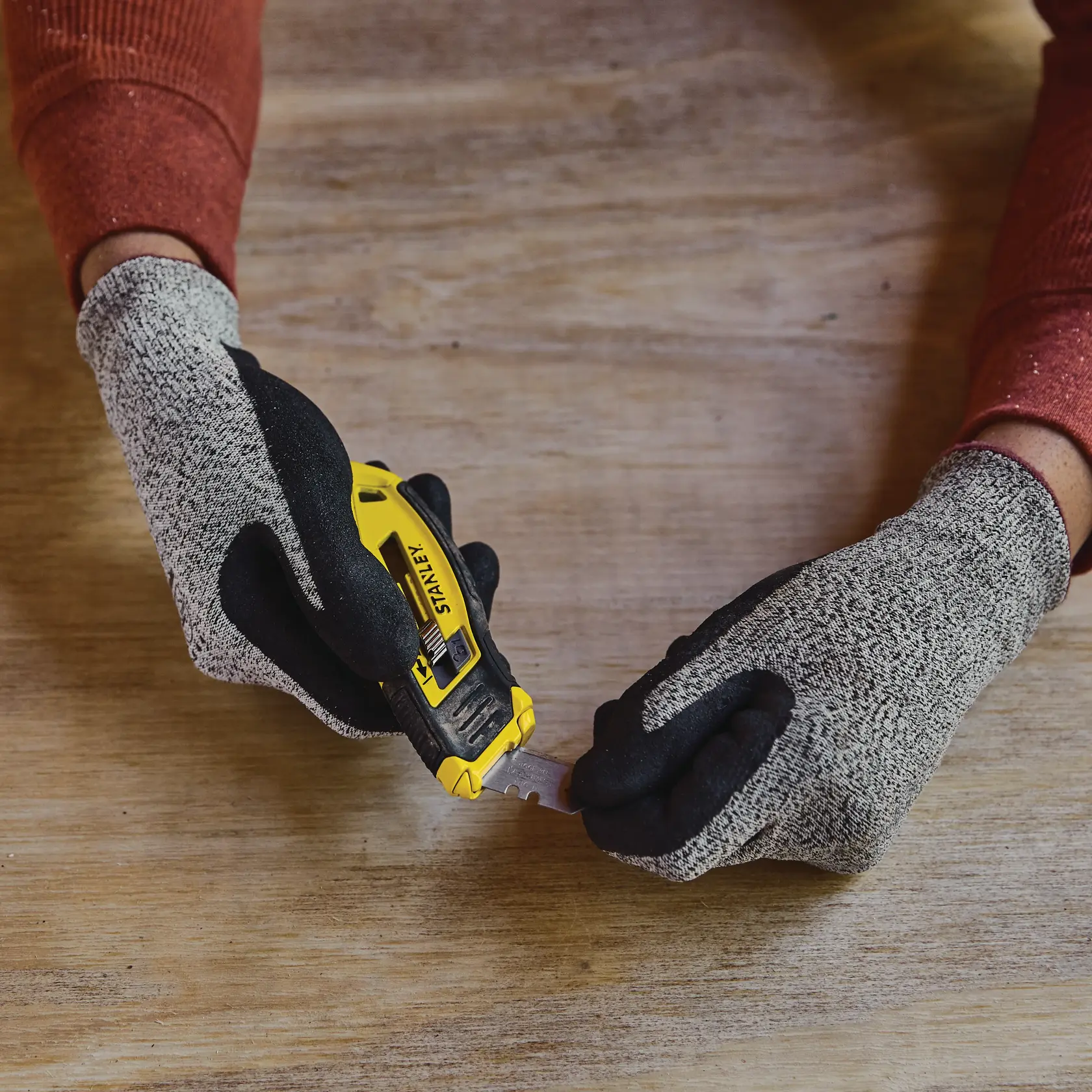 STANLEY STHT10432-0 utility knife held by gloved hands on a wooden table surface.