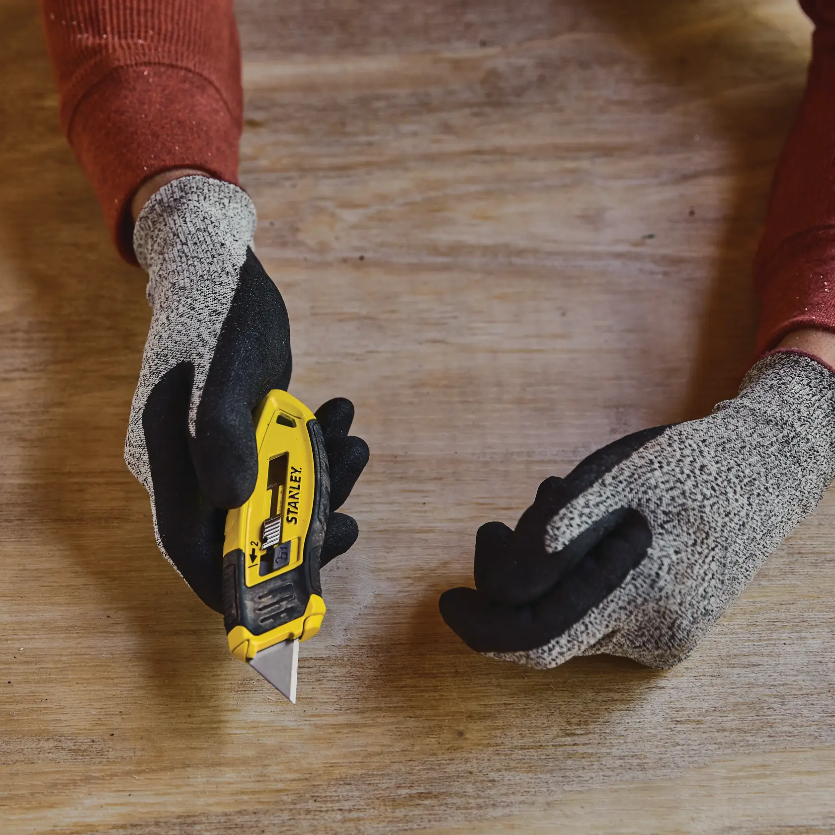 Photo of STANLEY STHT10432-0 utility knife held in gloved hand on wooden table.