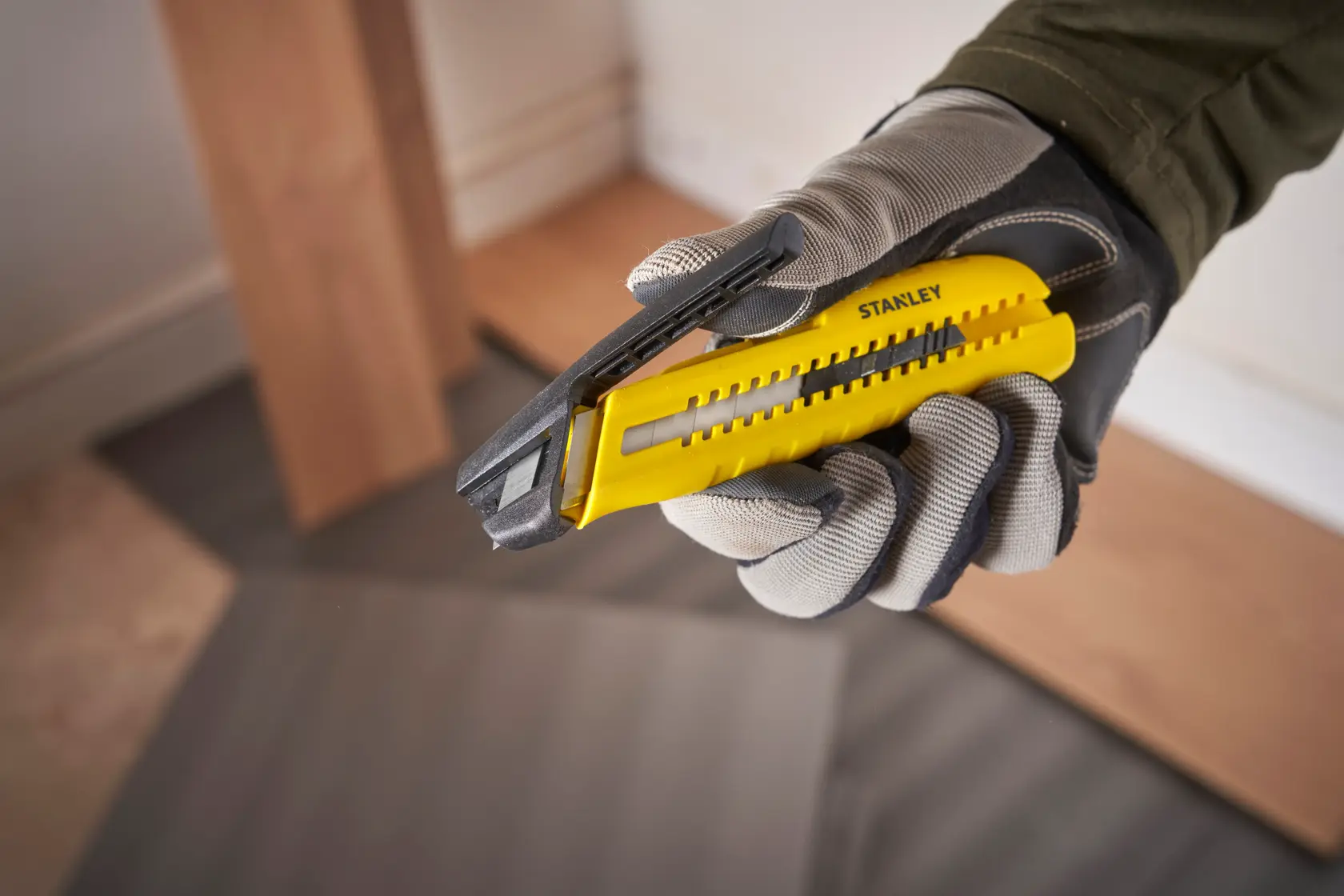 STANLEY STHT10489 Universalmesser mit gelbem und schwarzem Griff, behandschuhte Hand hält Werkzeug, schräge Ansicht.