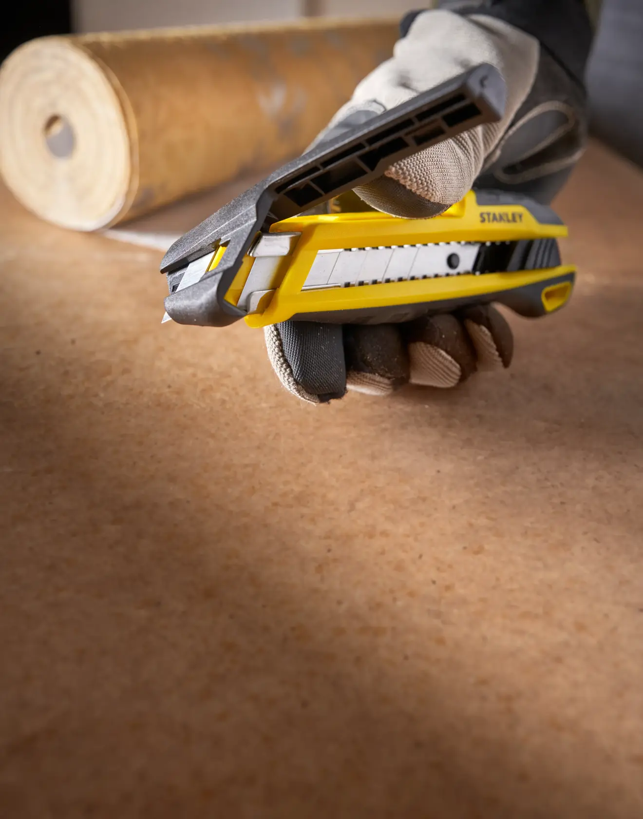 STANLEY STHT10501-0 utility knife in yellow and black held by gloved hand on work surface, side angle.