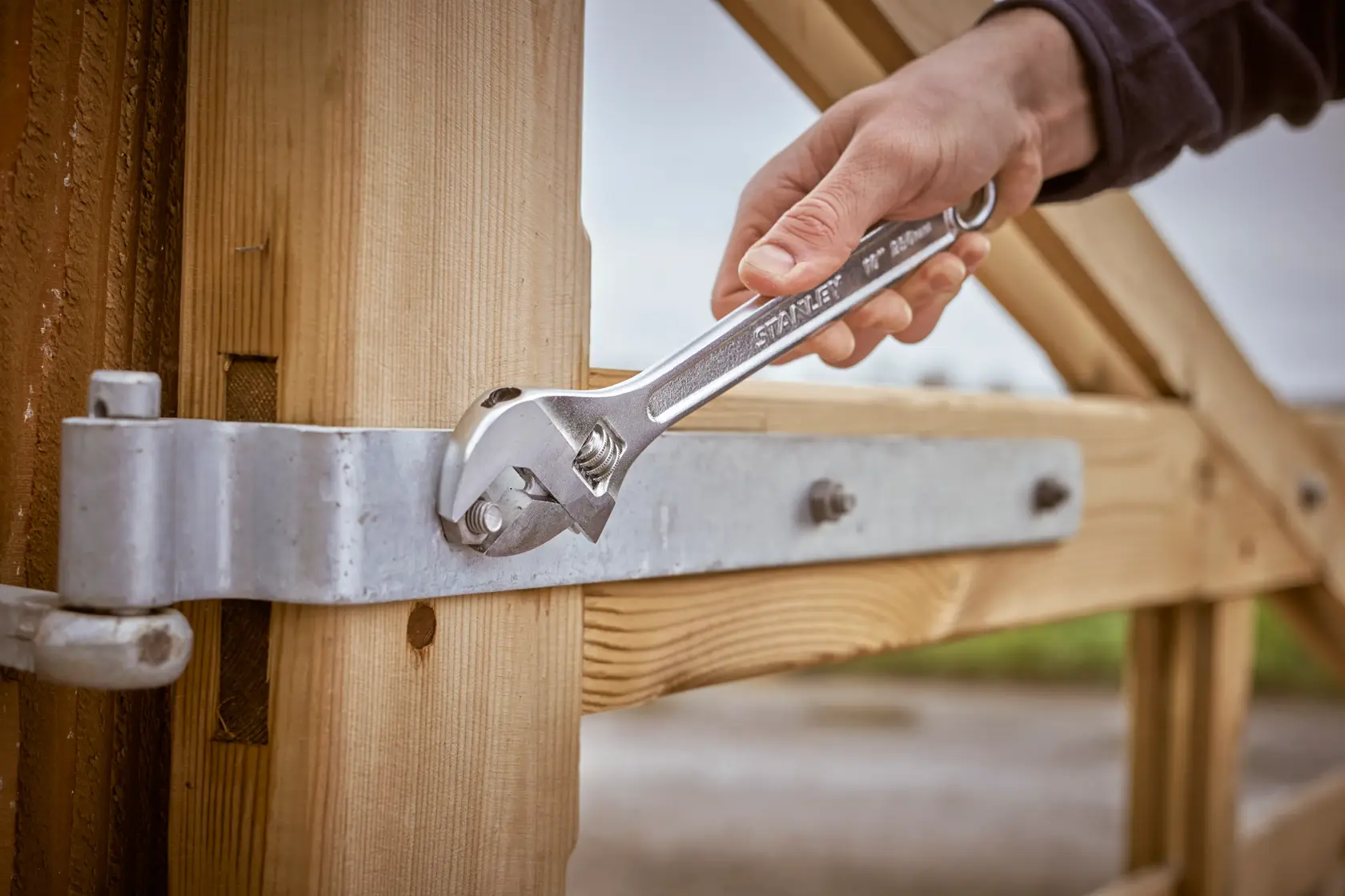 Photo of STANLEY STHT13123-0 adjustable wrench tightening a bolt on a metal hinge attached to a wooden gate.